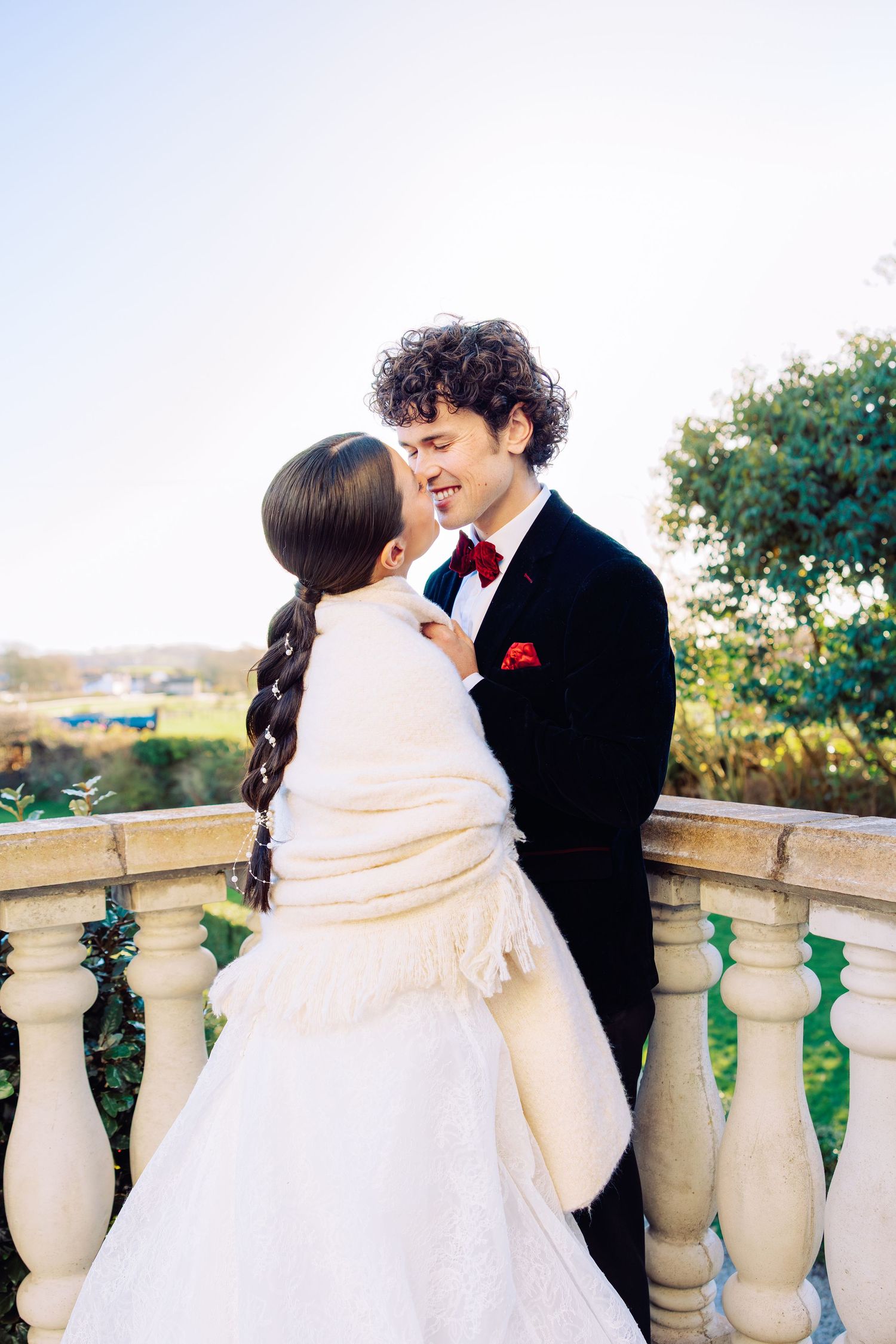 Romantic couple embraces on stone balcony during sunset wedding photoshoot.