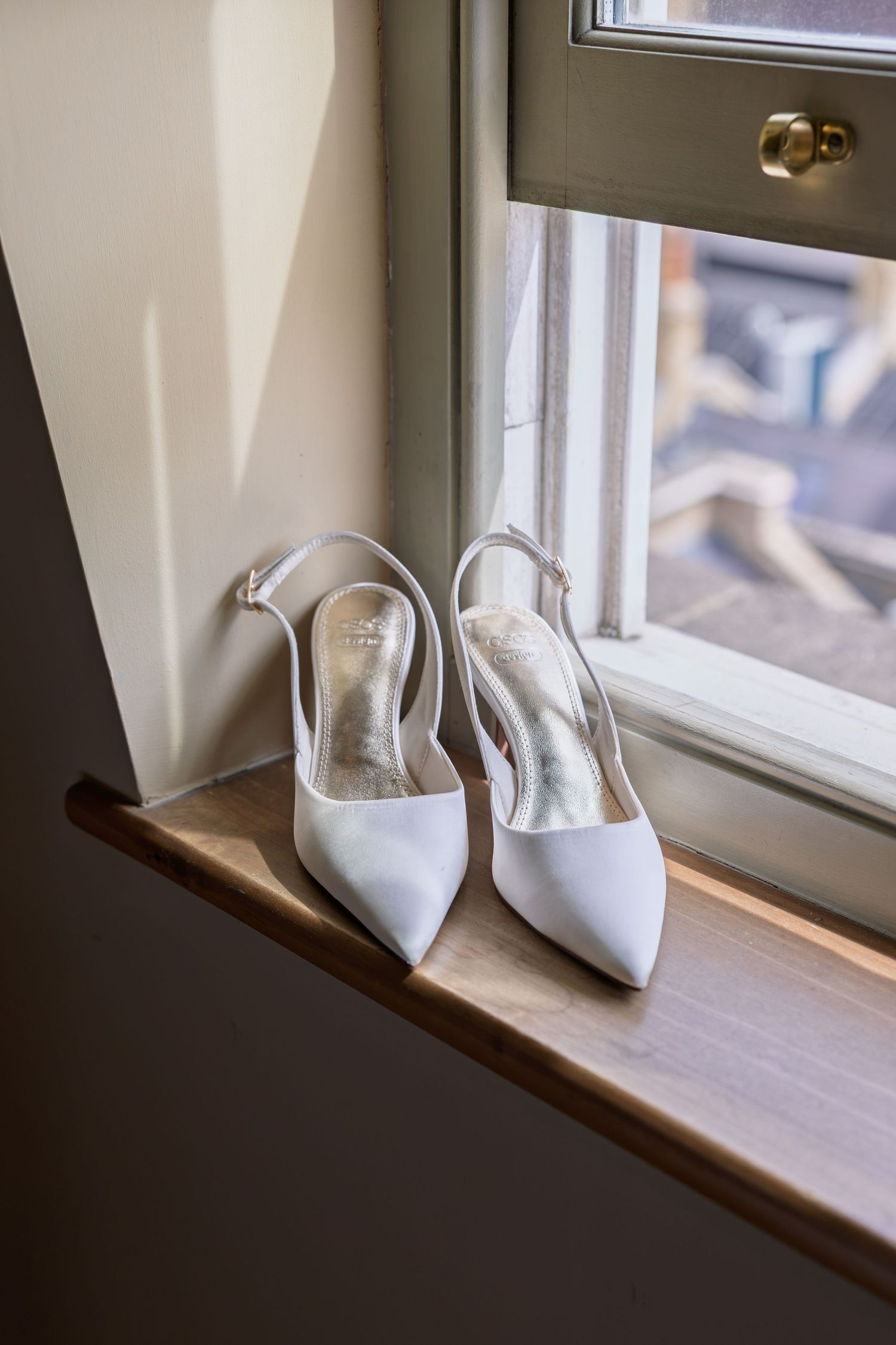 Elegant white satin slingback heels on a wooden windowsill, perfect bridal shoes for a wedding day.