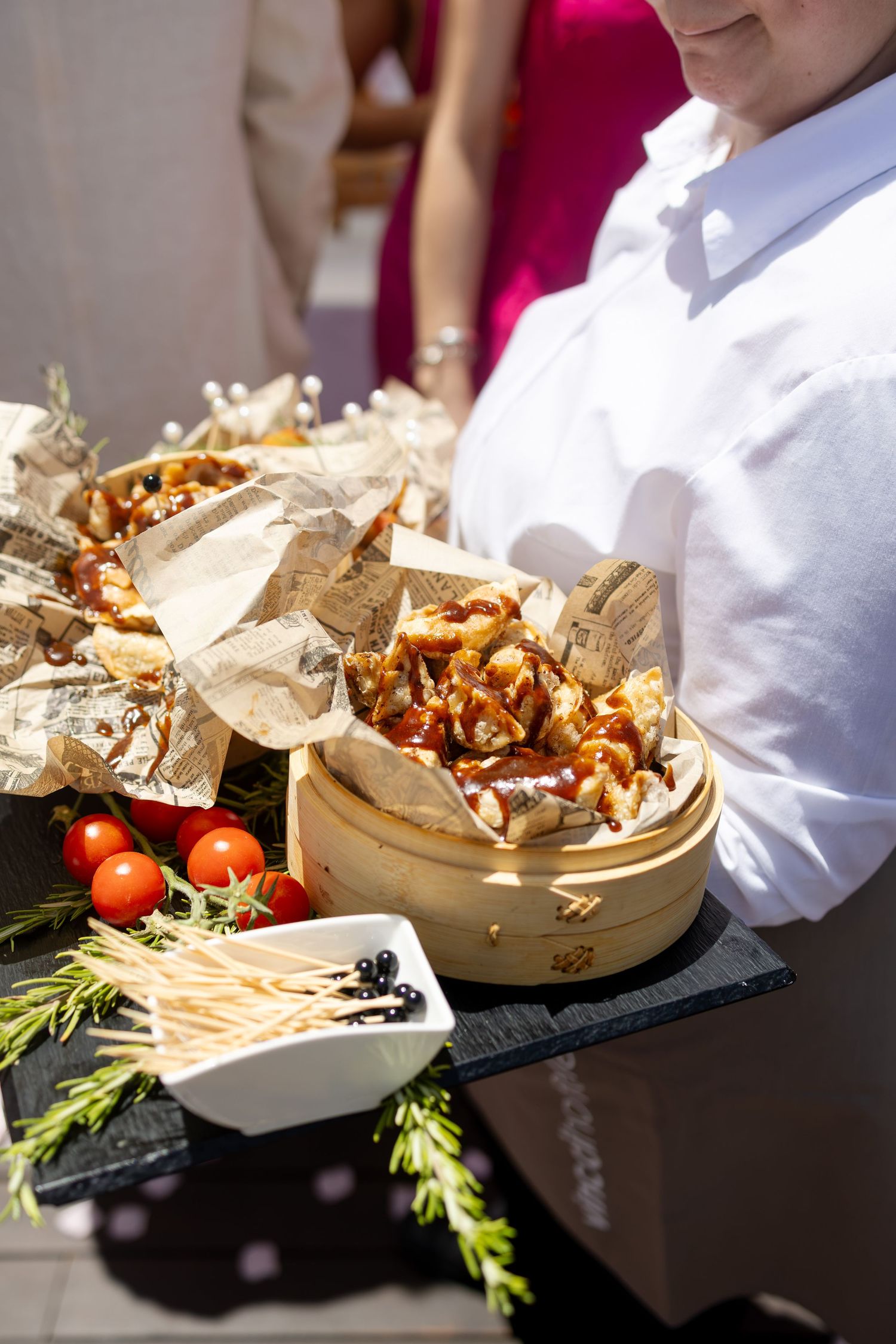 Waiter presents elegant appetizer platter with cherry tomatoes and garnishes at outdoor wedding reception.