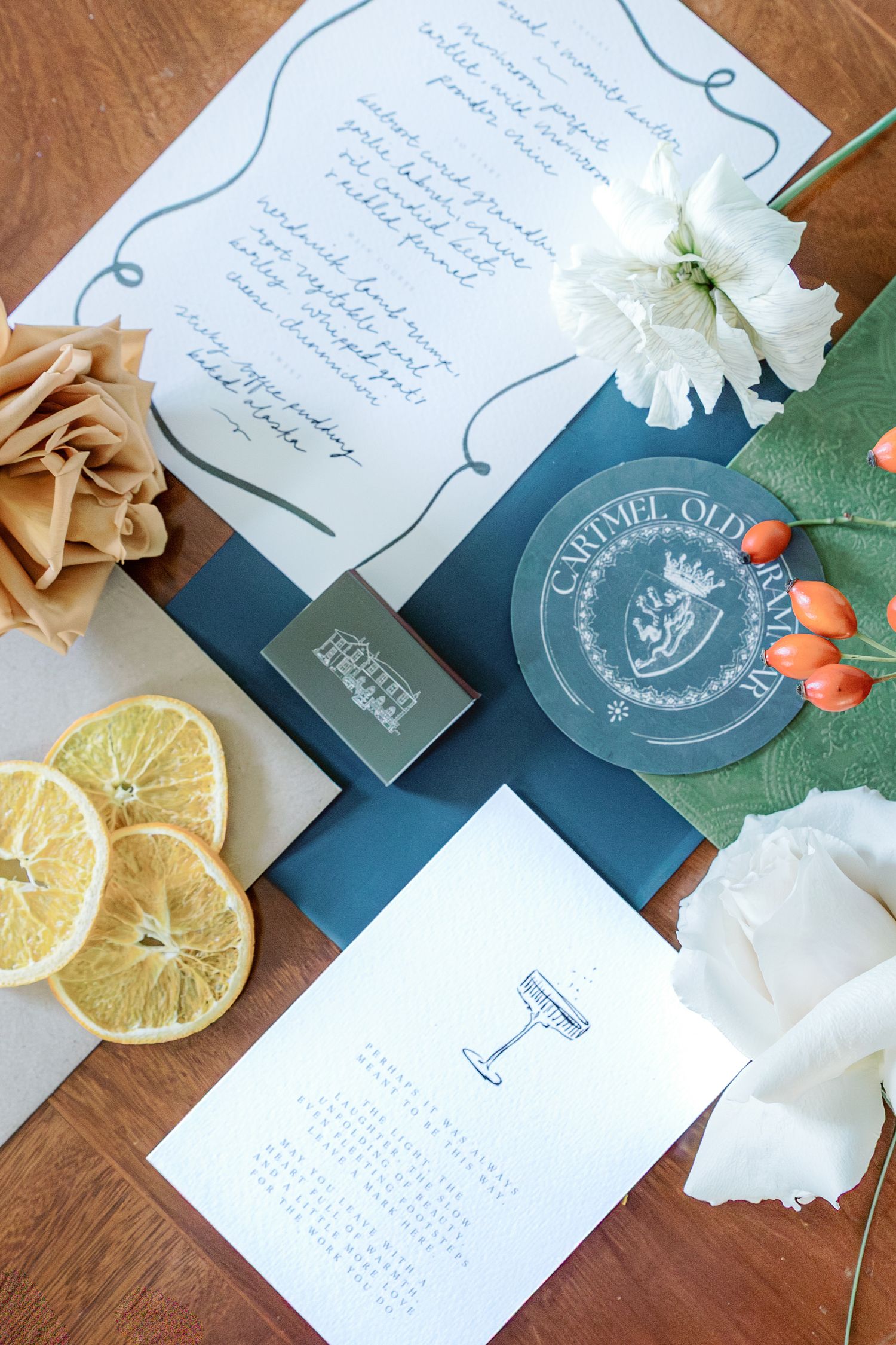 Wedding stationery set with blue accents, dried citrus slices and floral details on wooden surface.