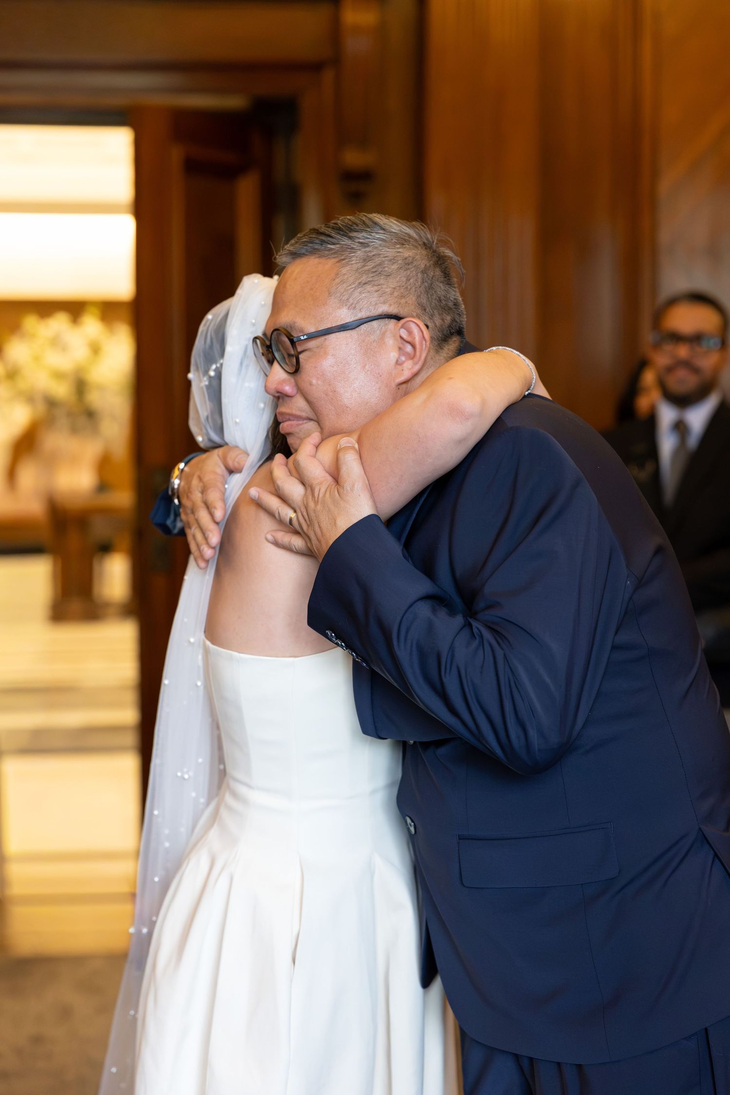 Emotional father embracing bride in wedding dress and veil at ceremony.