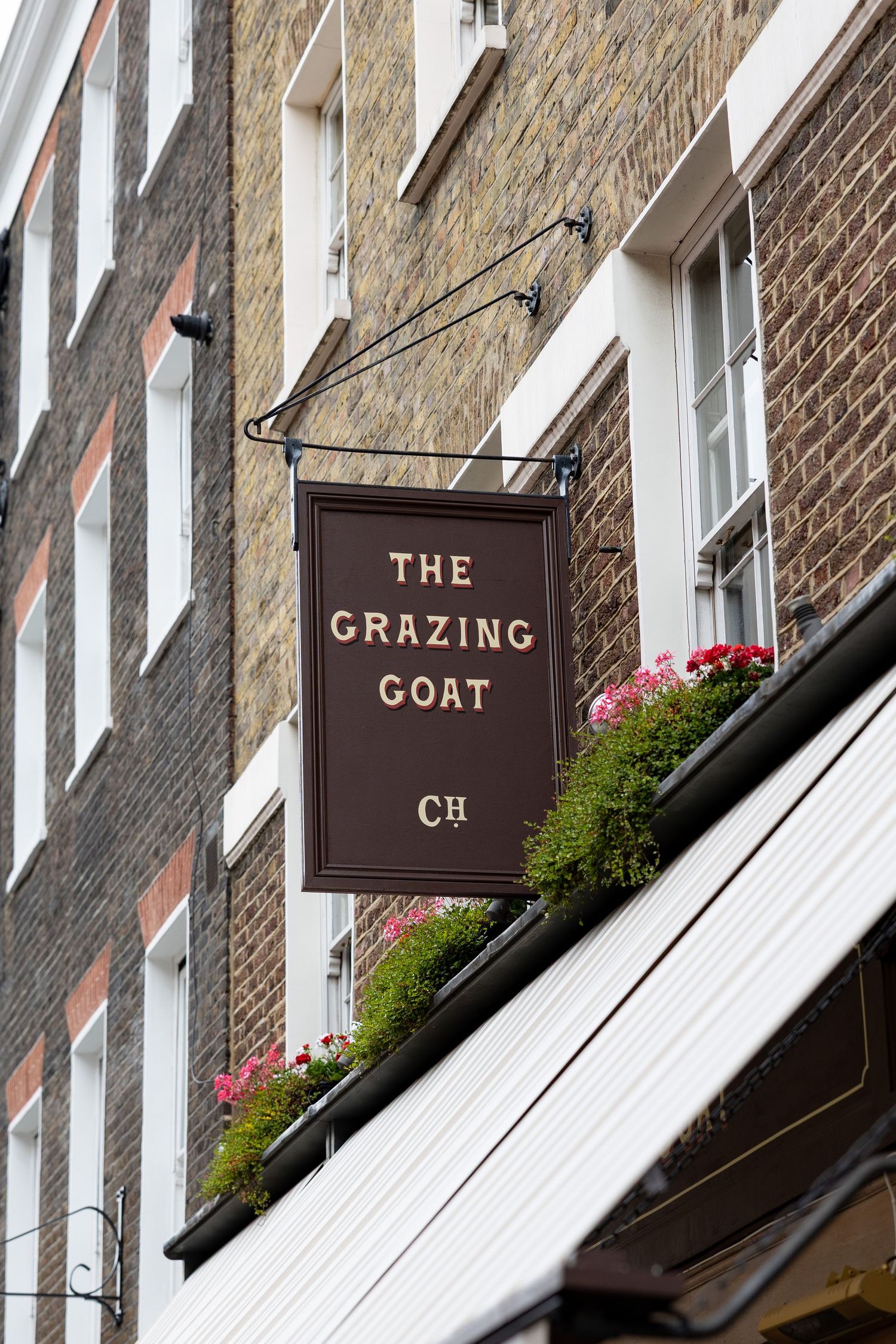 The Grazing Goat pub sign mounted on a brick building facade with flower boxes below.