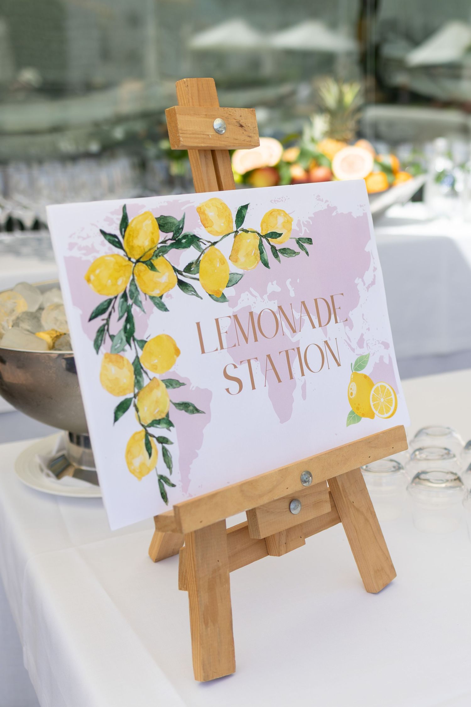 Charming lemonade station sign with lemon watercolor artwork on wooden easel at wedding.