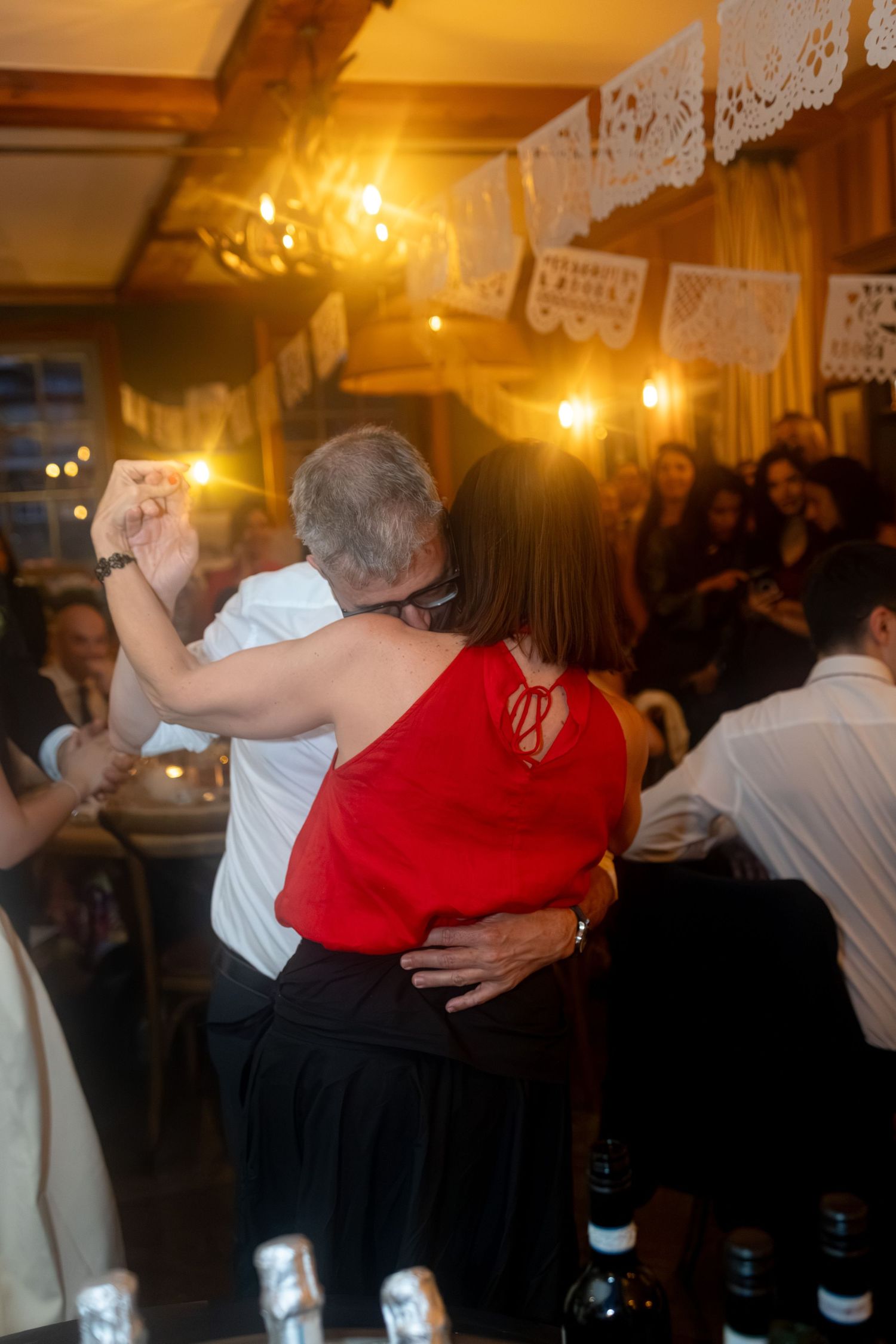 Couple dancing closely together at a festive wedding reception with papel picado decorations and warm lighting.