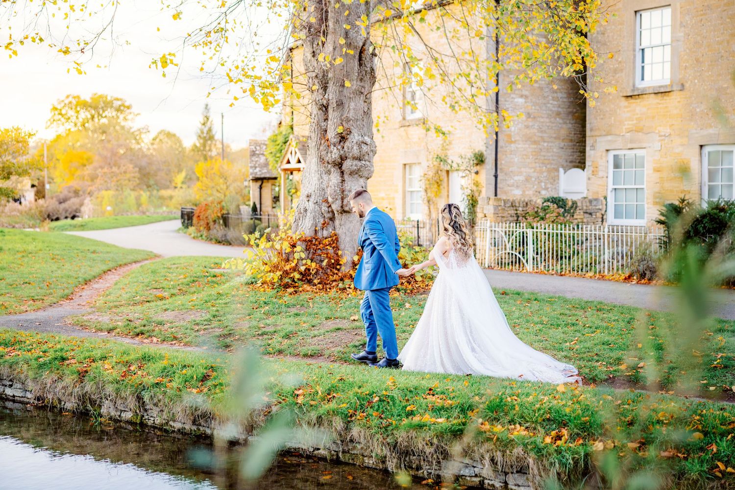 A couple in wedding attire poses for romantic photos along a stone path surrounded by autumn foliage.