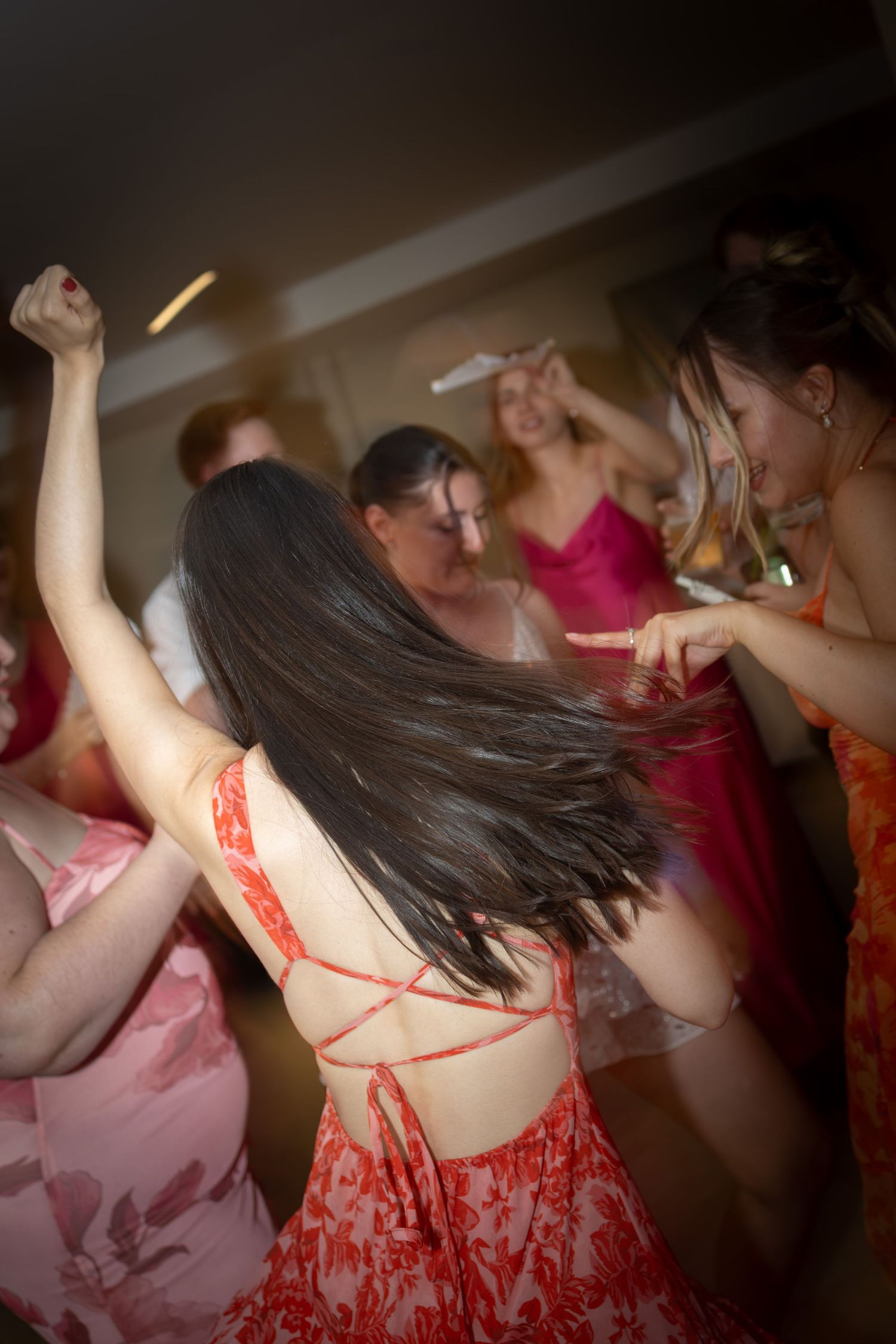 Woman in red backless dress dances energetically with guests at lively wedding reception.