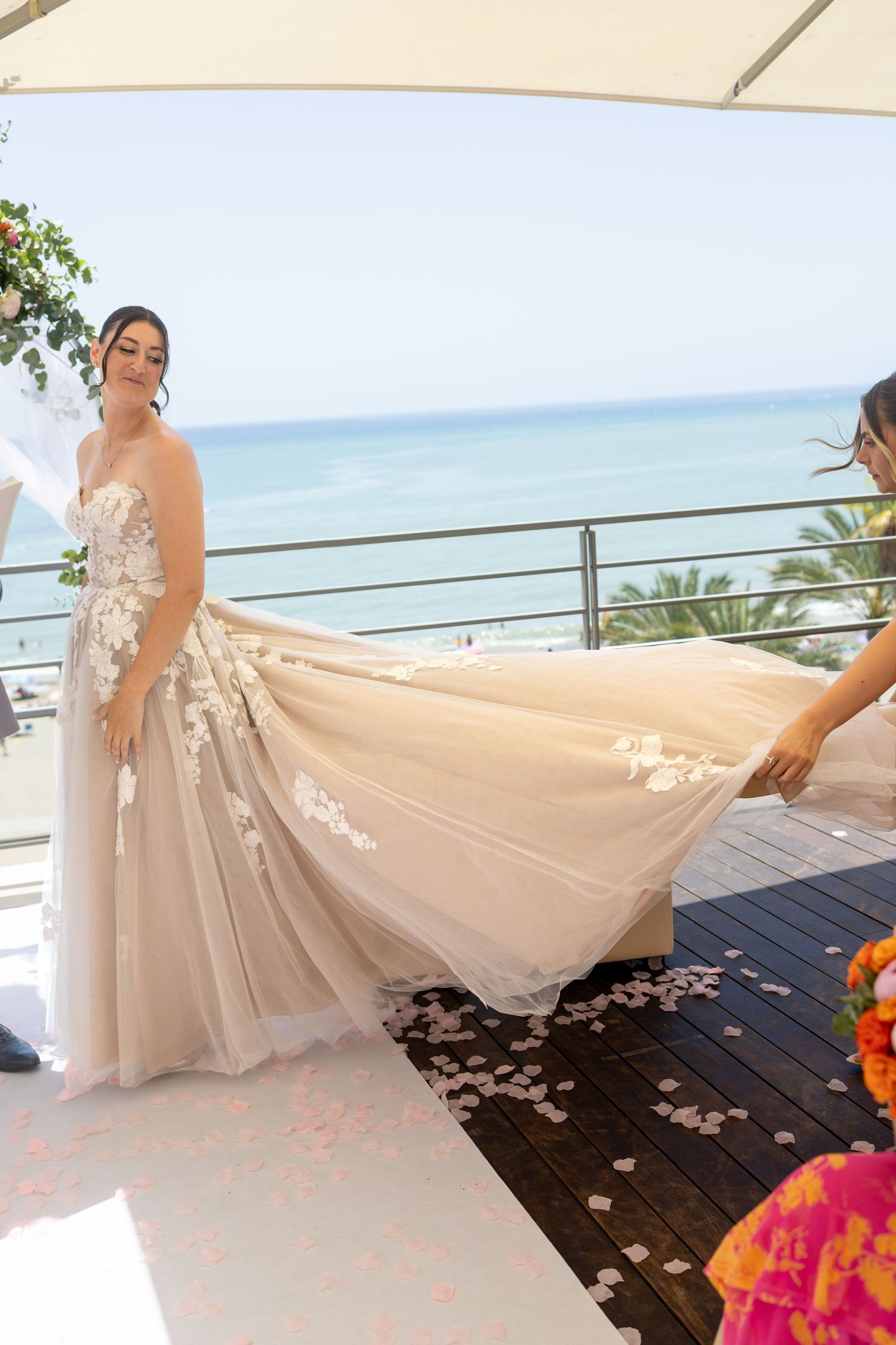 Bride in floral tulle wedding gown having her train arranged at a beachfront wedding ceremony.