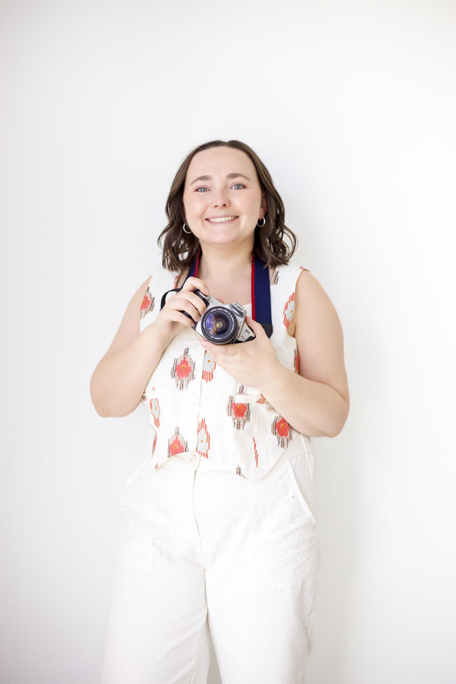Photographer with camera and navy strap posing against white background.