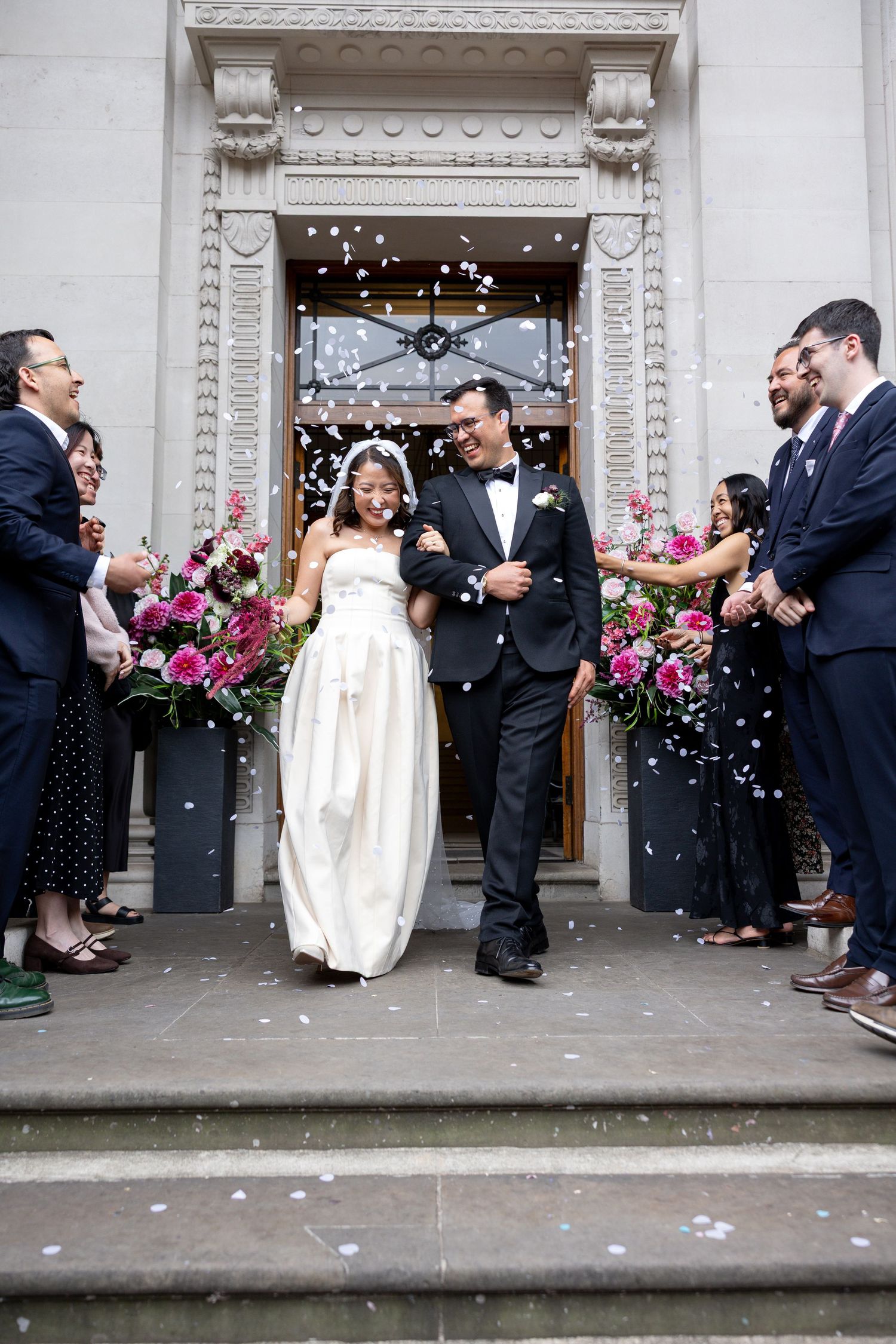Bride and groom exit church doors as guests throw white confetti during wedding celebration.
