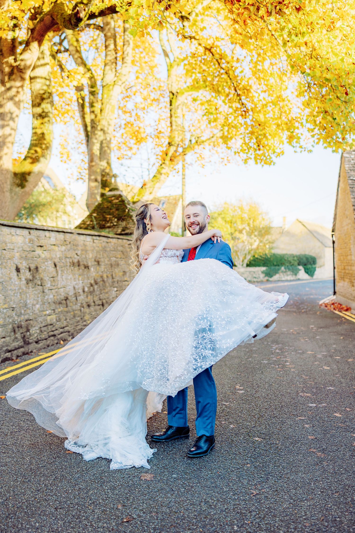 Bride and groom dancing playfully on path with autumn leaves.