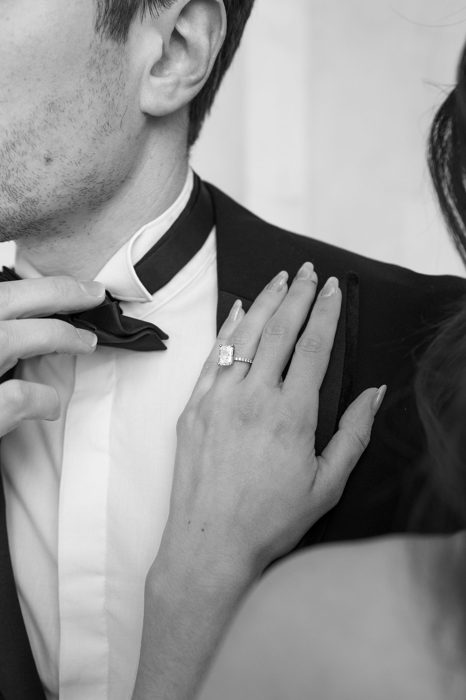 Close-up black and white photo showing hands adjusting a bow tie and a diamond ring.