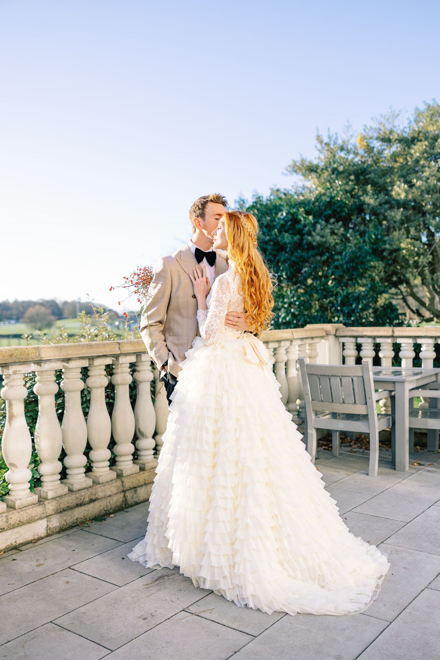 Elegant wedding couple shares romantic moments on a stone balcony with scenic countryside views in the background.