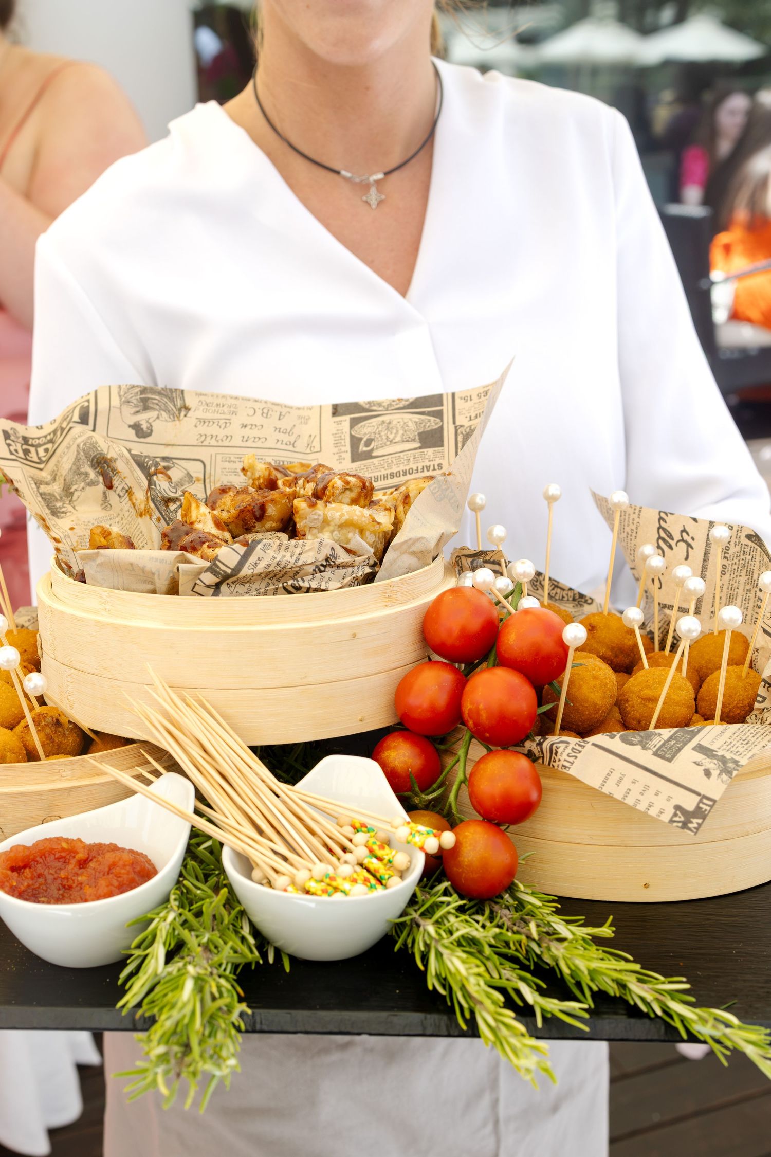 Wedding catering display with appetizers, cherry tomatoes on skewers, dipping sauces, and rosemary garnish.