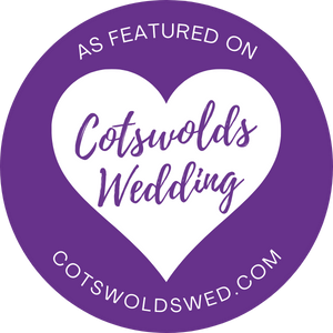 A purple circular badge with a white heart featuring 'Cotswolds Wedding' text and website for featured vendors.