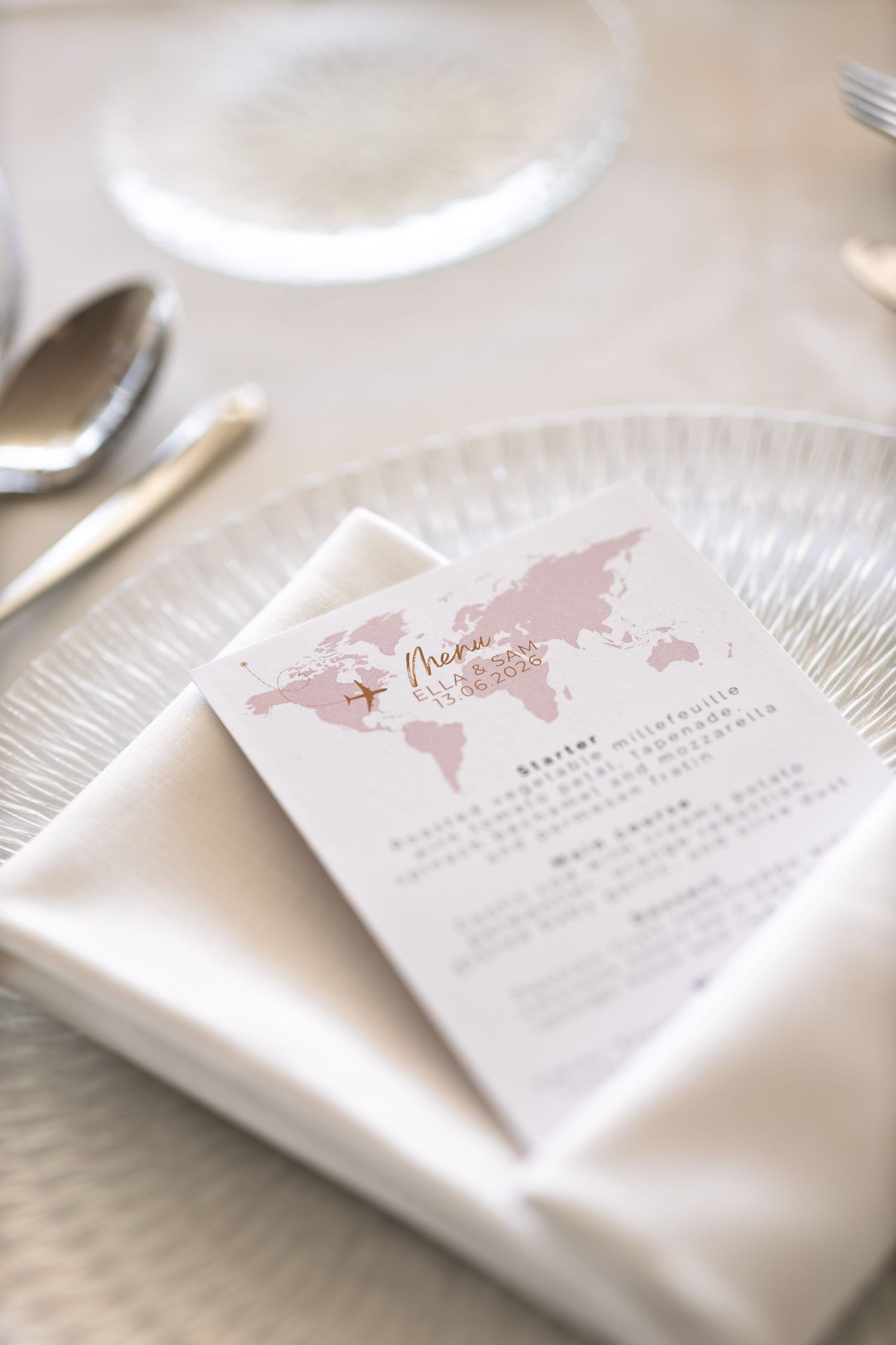 Elegant wedding menu card with pink world map design on white napkin at a formal place setting.