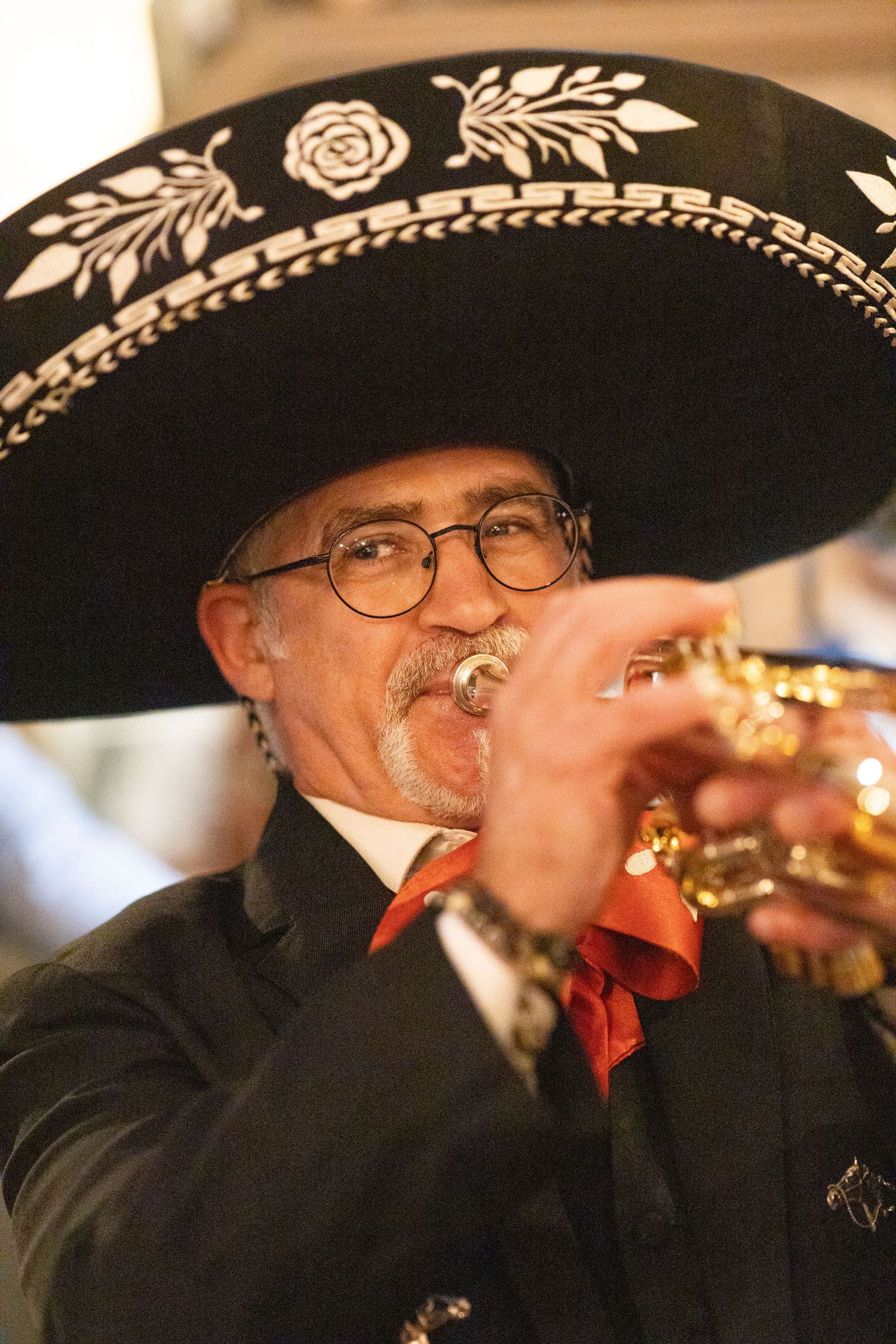 Mariachi musician in traditional black sombrero plays trumpet at a lively wedding celebration.