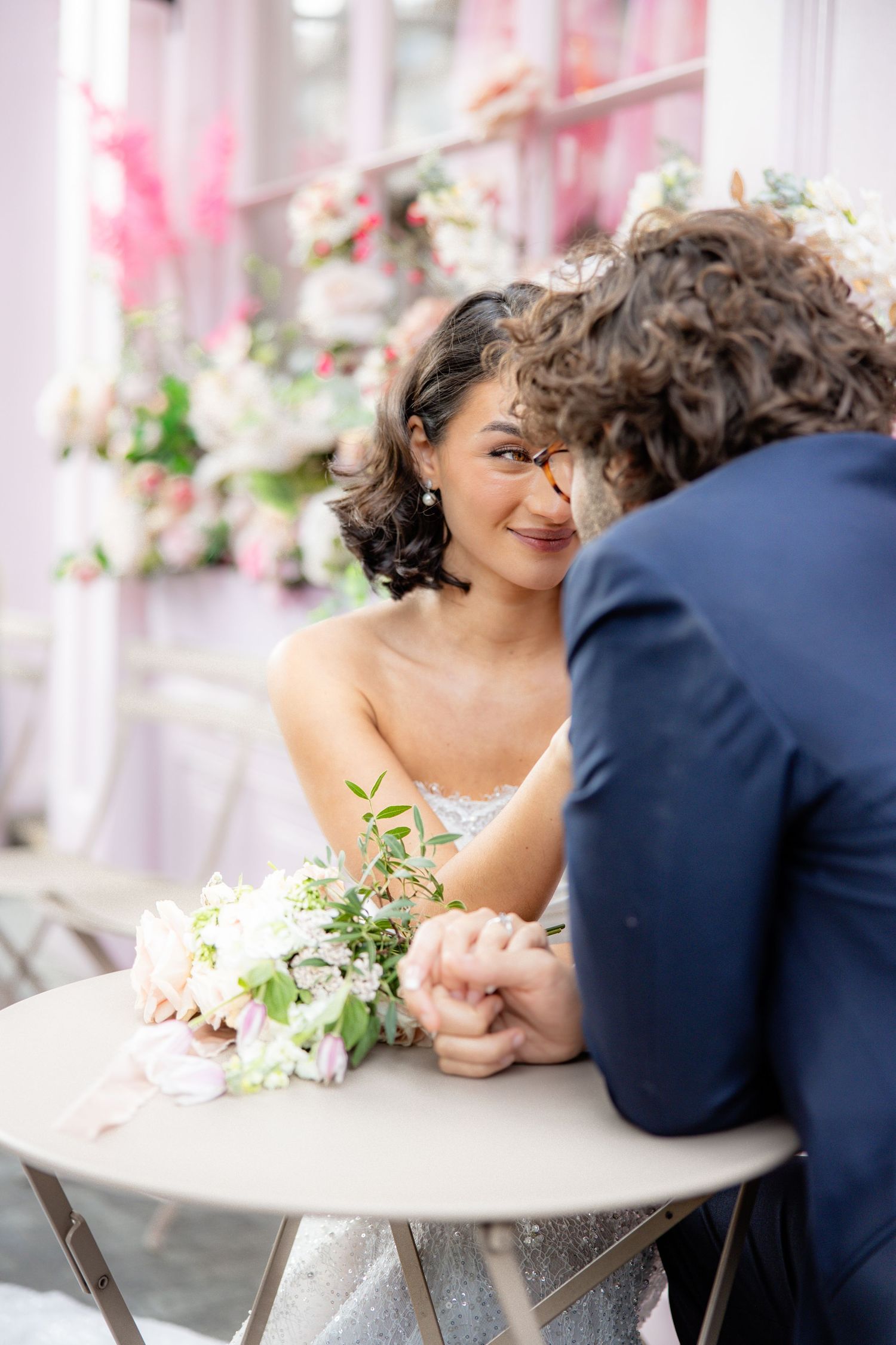 Intimate wedding moment captured at cafe table with pink floral decorations.