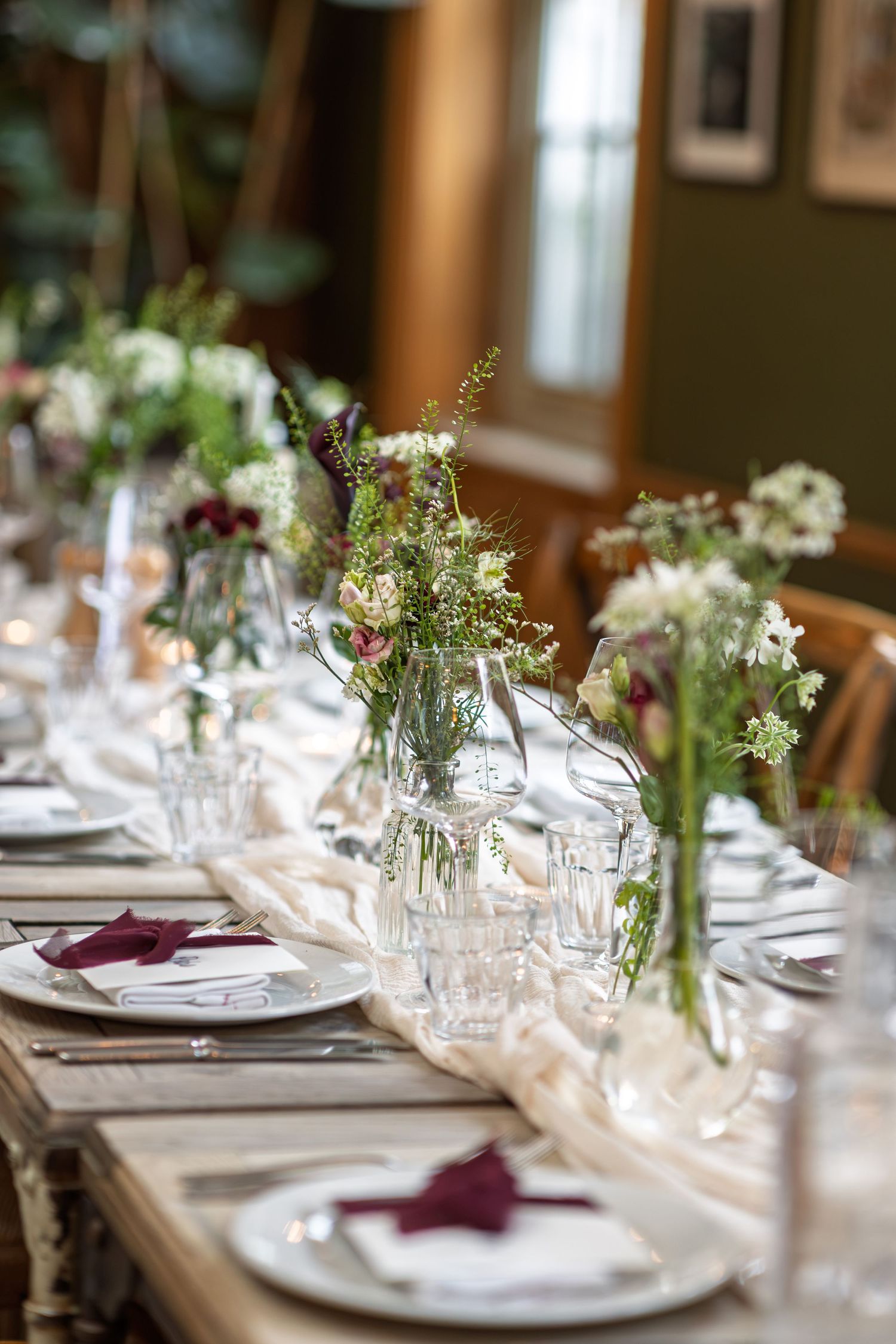Elegant wedding reception table with wildflower centerpieces, burgundy napkins and crystal glassware.