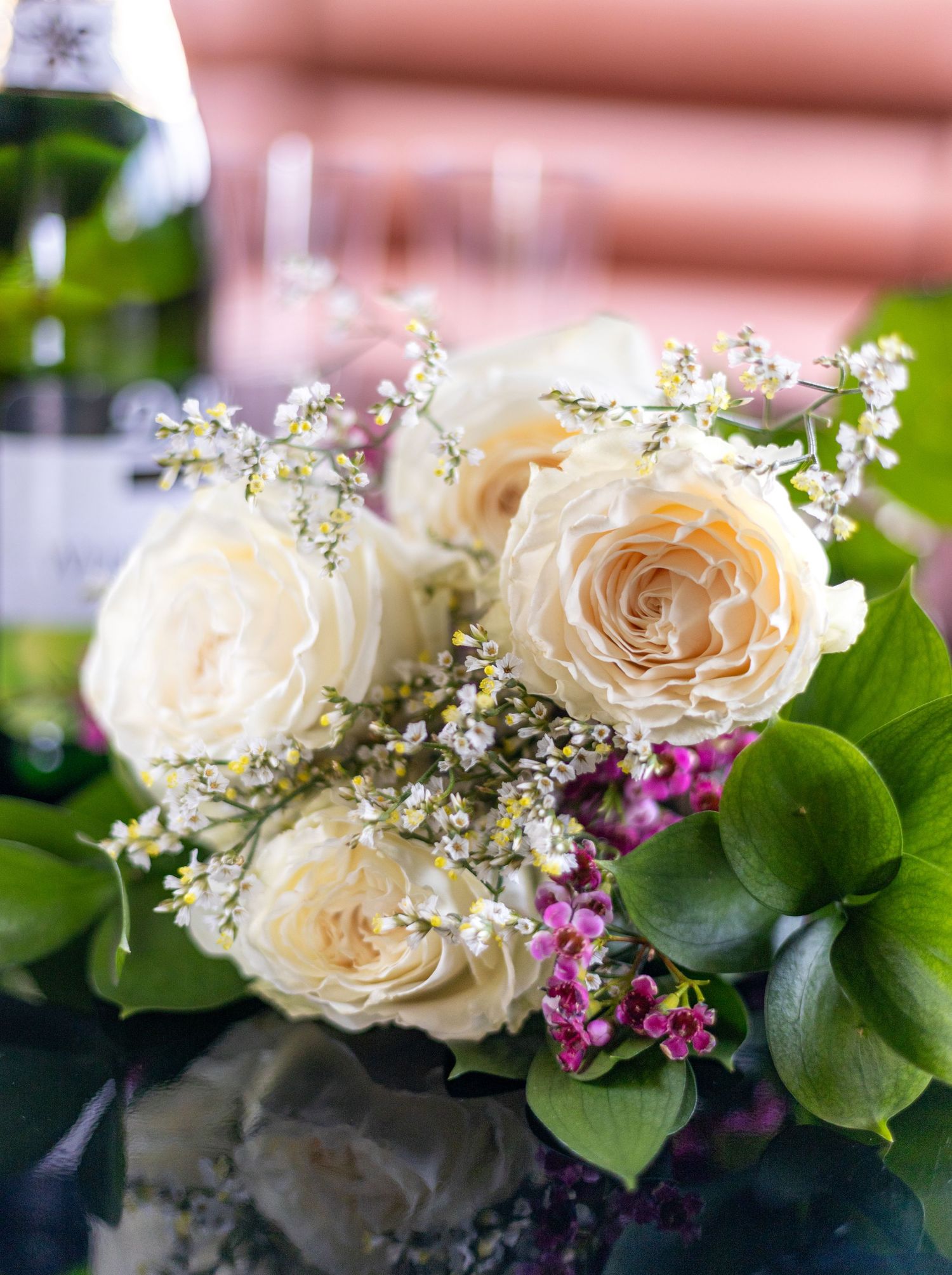 Elegant cream roses and delicate baby's breath arranged in a floral wedding centerpiece with green foliage.