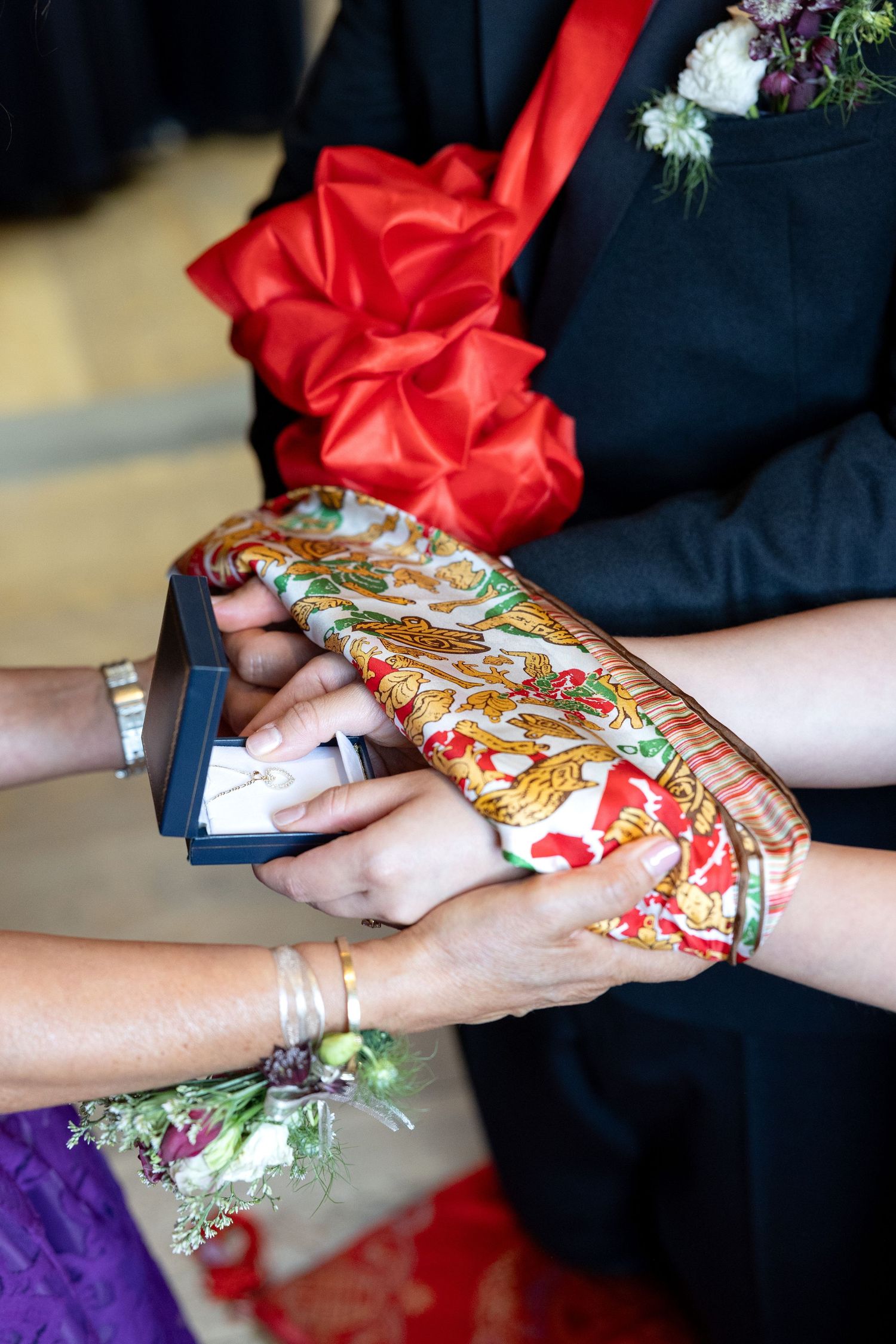 Hands exchanging wedding rings on colorful batik fabric during a traditional ceremony.