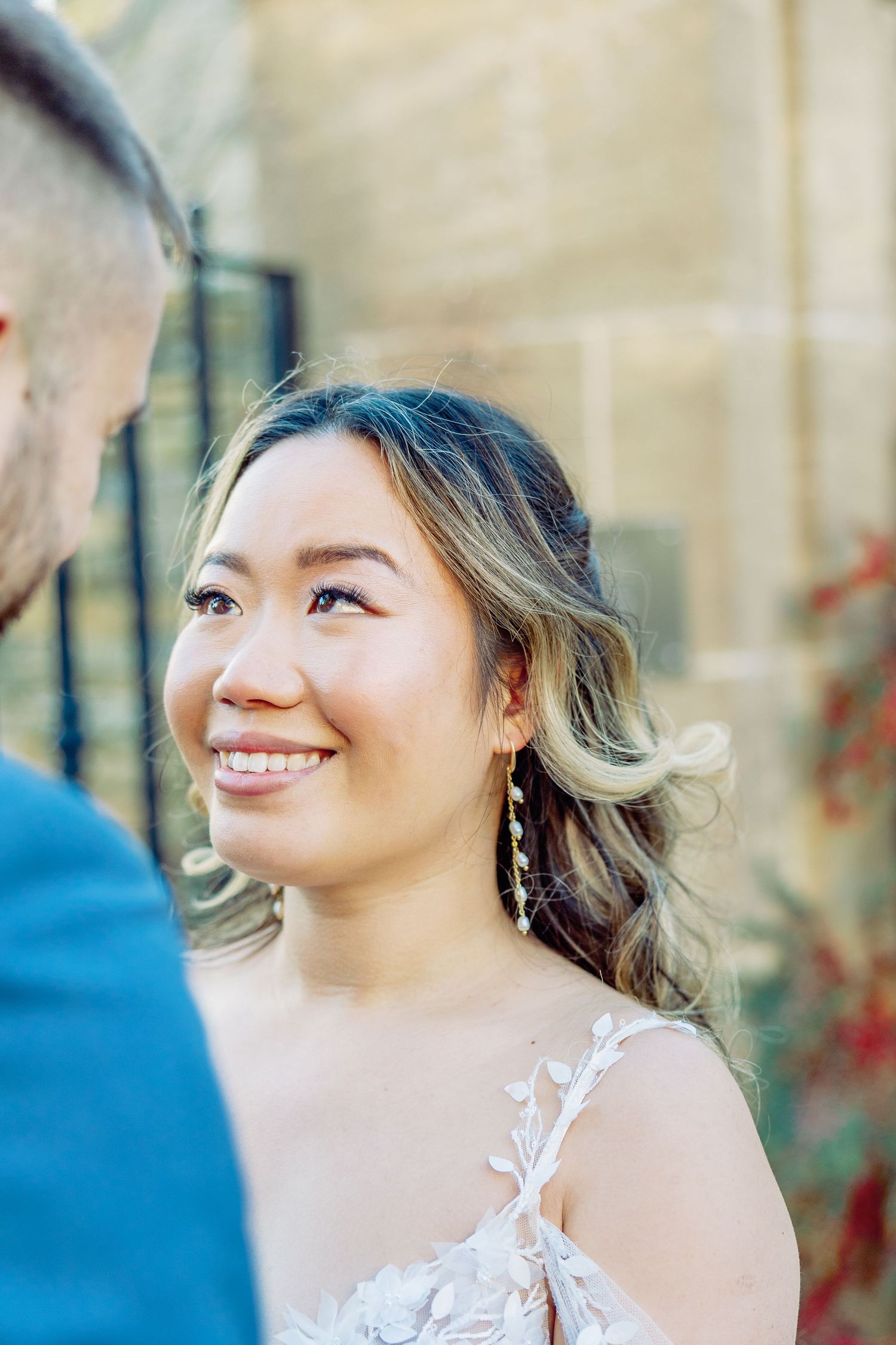 Bride smiling joyfully in white lace dress during outdoor wedding portraits.