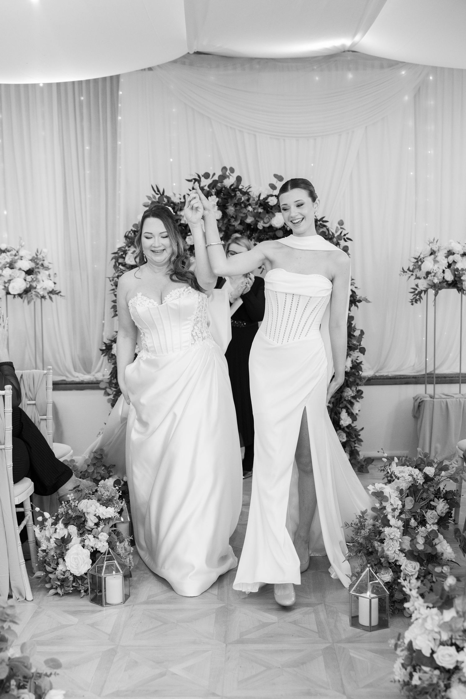 A series of white wedding dresses displayed with floral arrangements against a light backdrop in a bridal boutique setting.