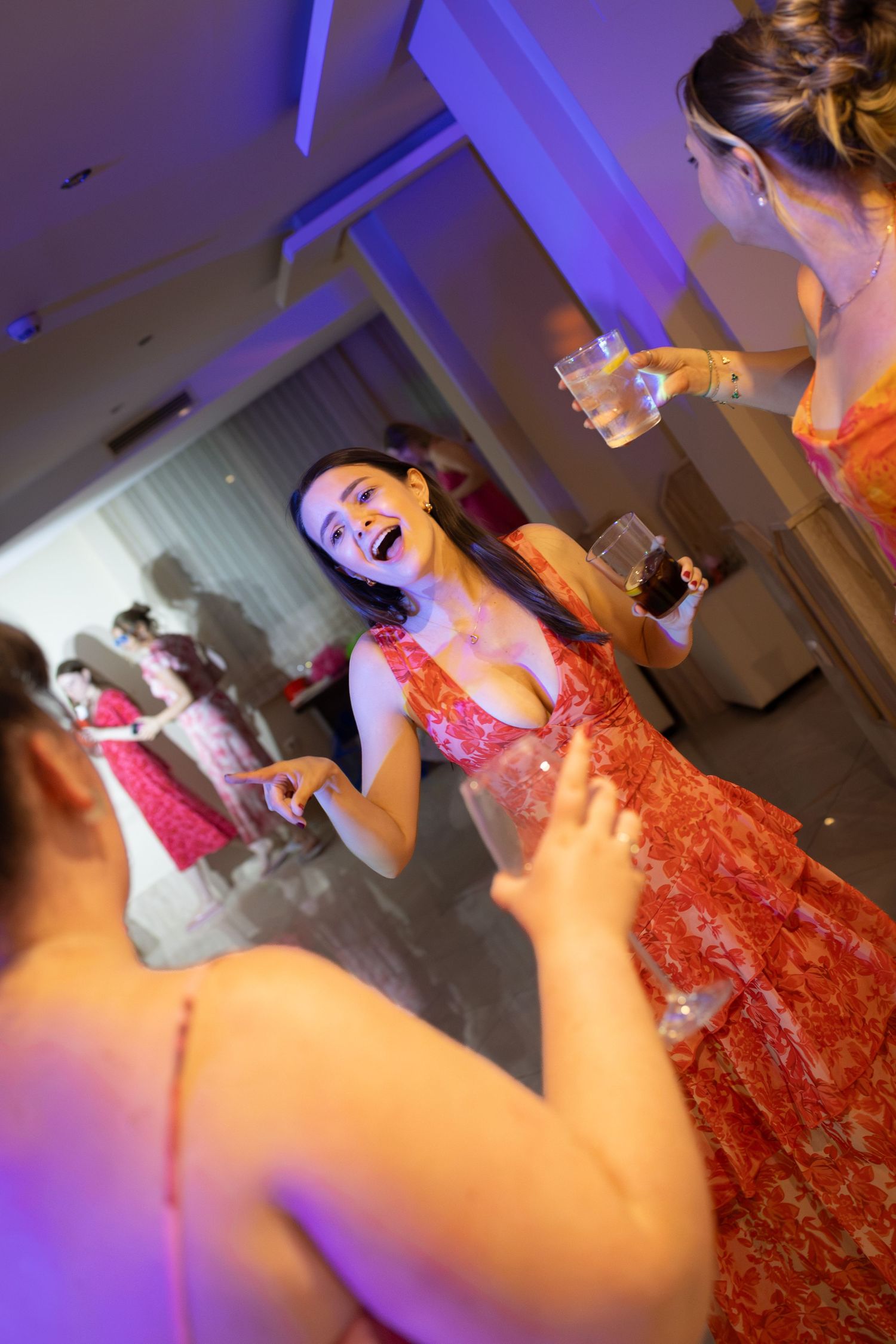 Joyful bridesmaid in red floral dress laughs and dances at wedding reception party.