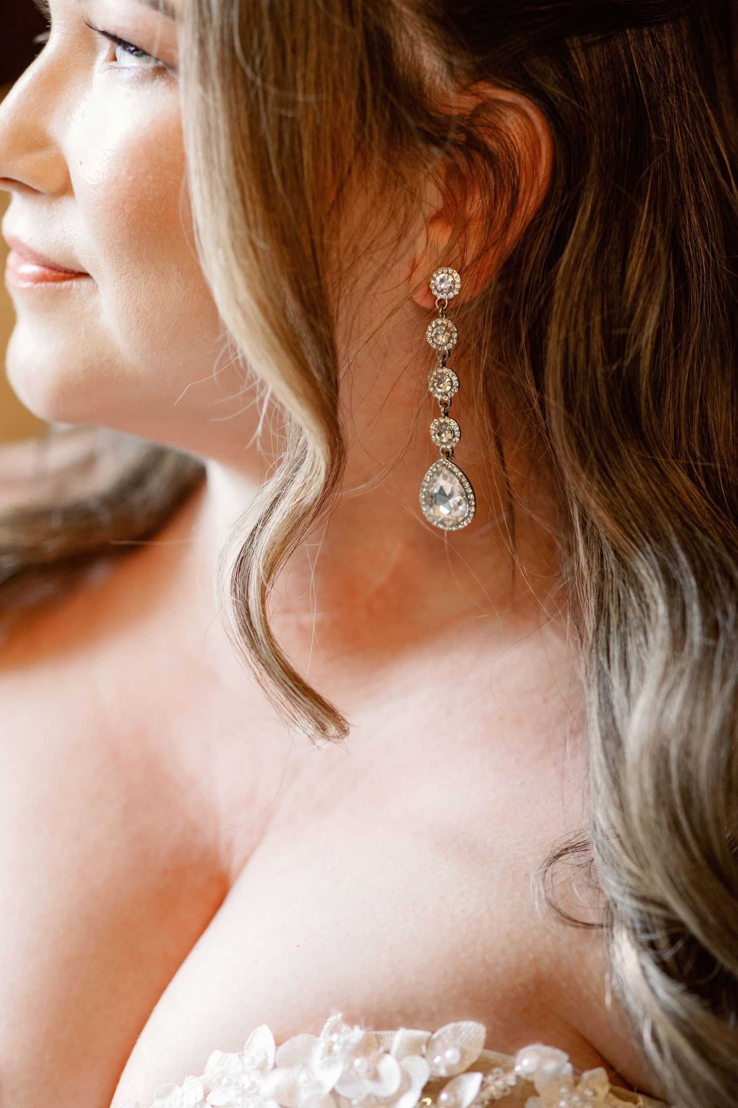 Close-up view of sparkling crystal drop earrings with elegant curled hair against a soft blurred background.
