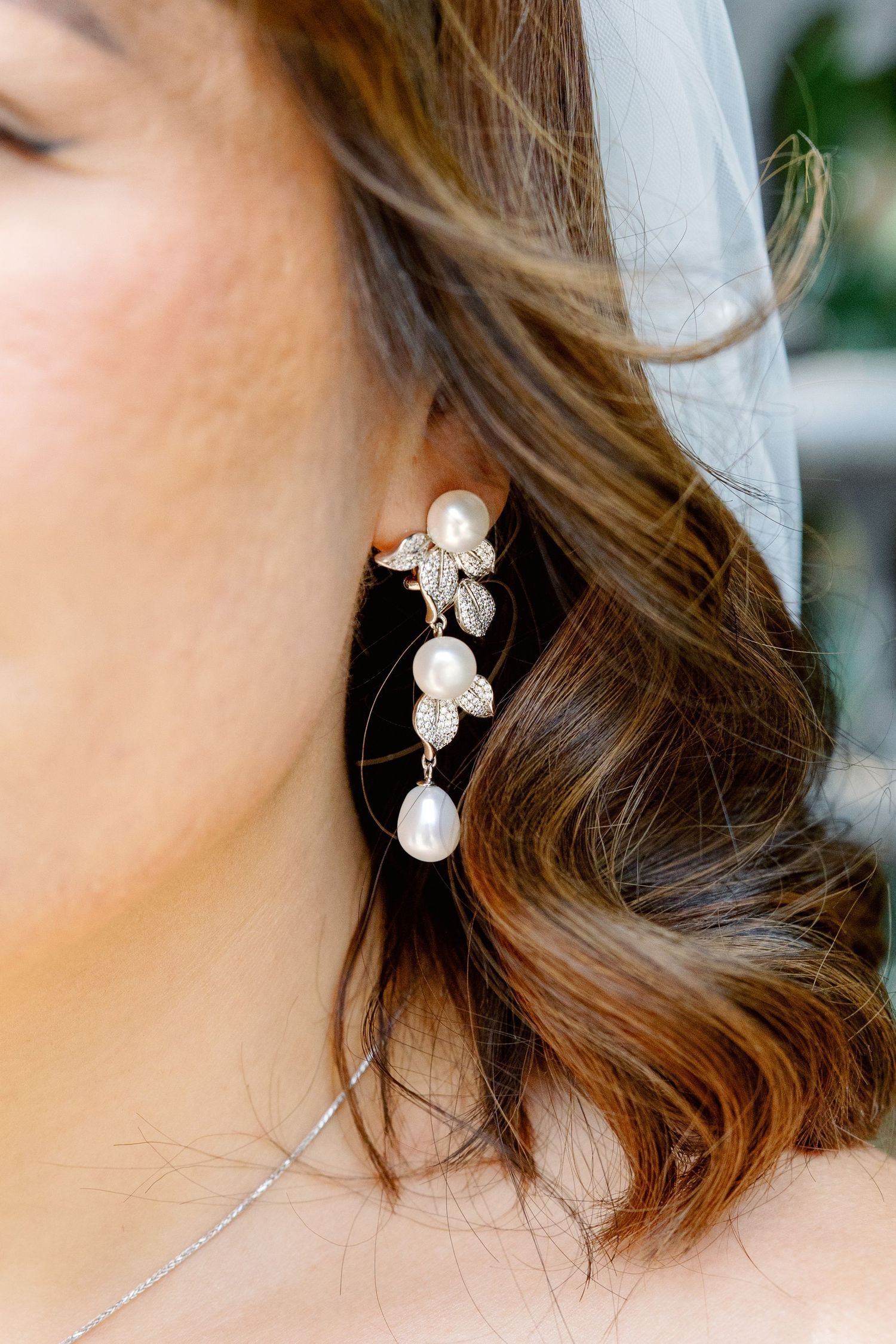 Close-up of a bride wearing elegant pearl and crystal drop earrings with a white wedding veil.