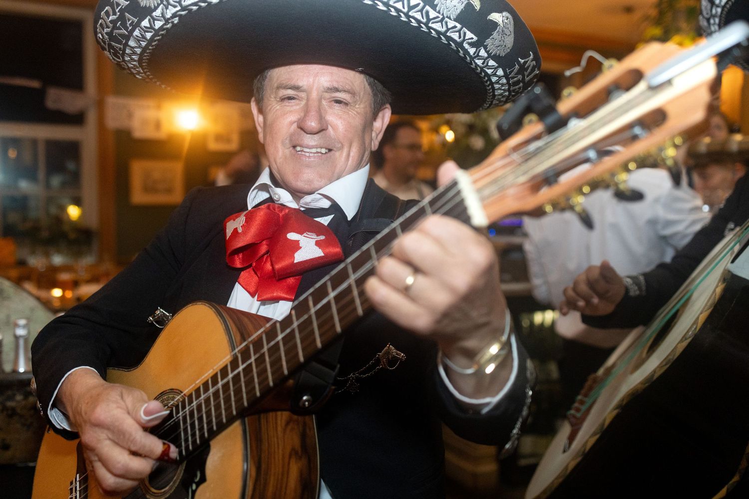 Mariachi musician in traditional sombrero plays guitar at lively wedding celebration.