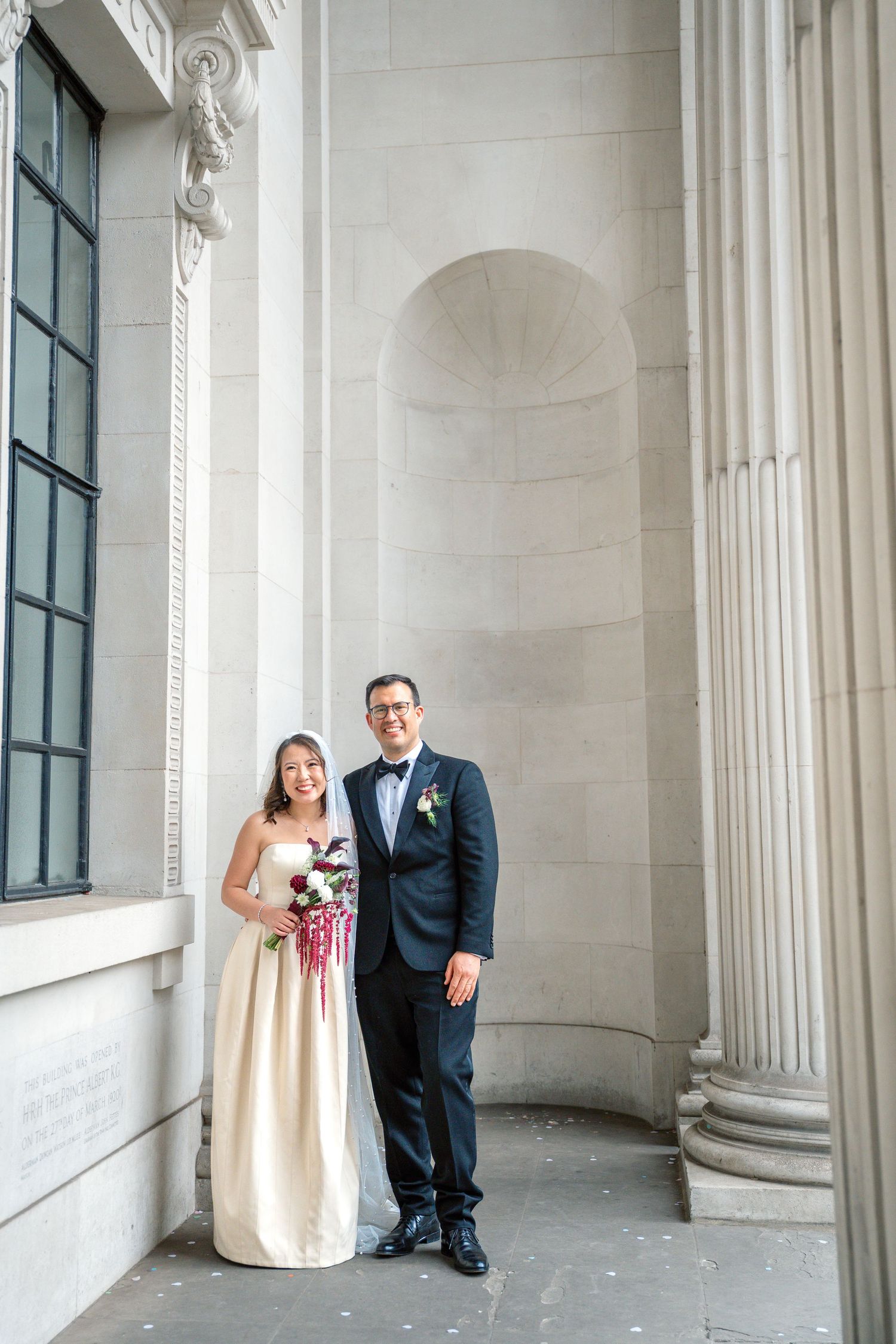 Bride and groom posing together at neoclassical building with stone columns.