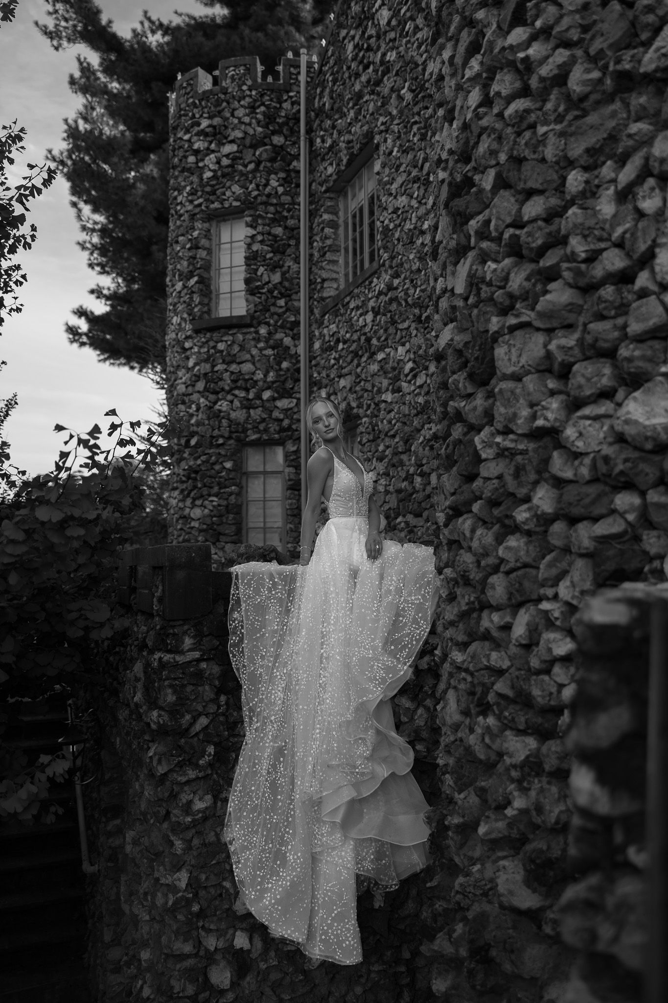 Wedding dress hanging outdoors against a rustic stone wall in dramatic black and white.