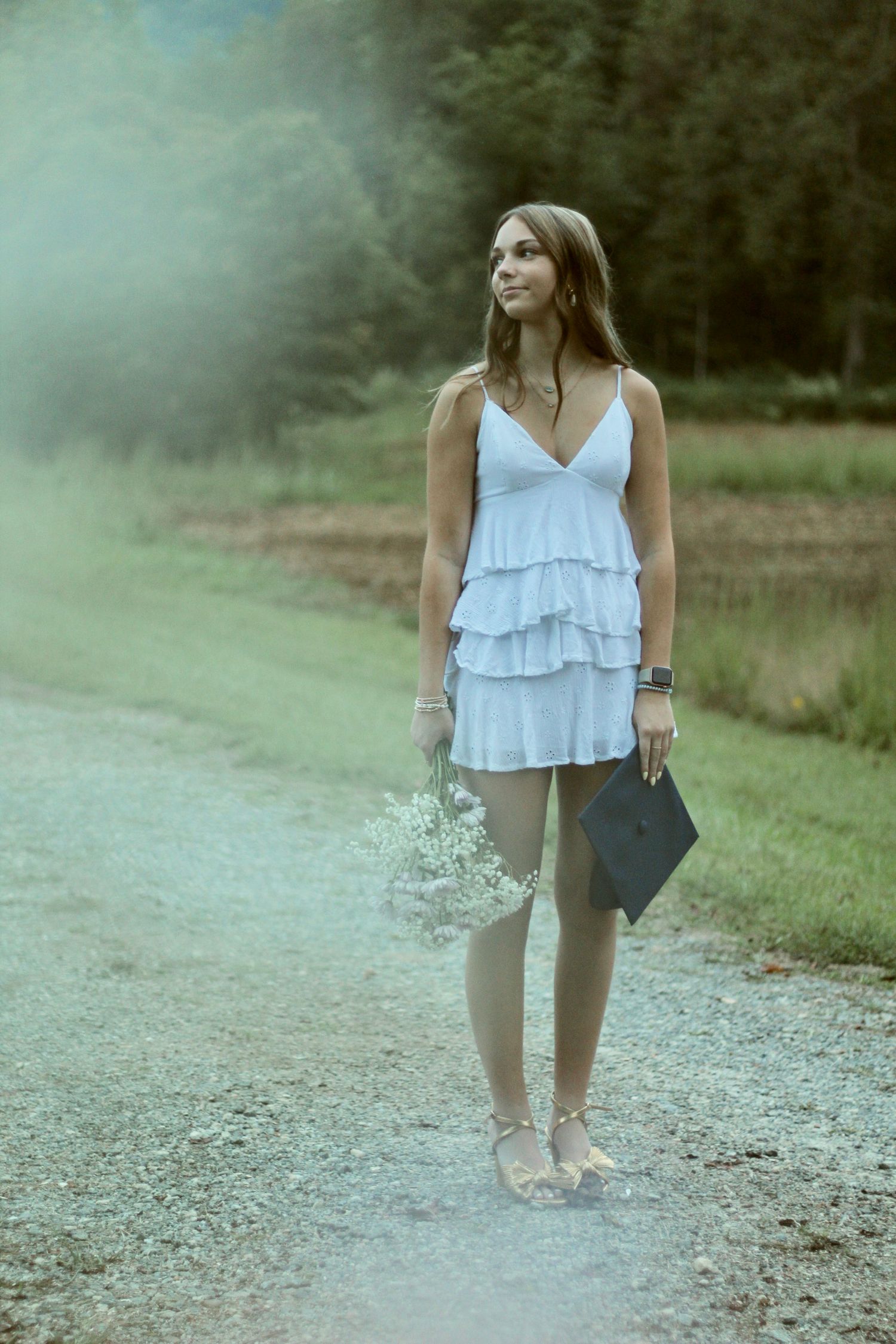 She's looking off into the distance thinking about her future as she holds onto her cap and bouquet.