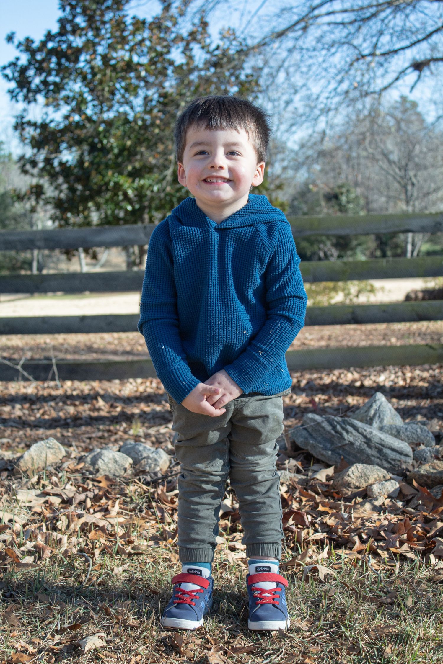 He's just laughing right at the camera. Young boy smiling at camera with trees in the background.