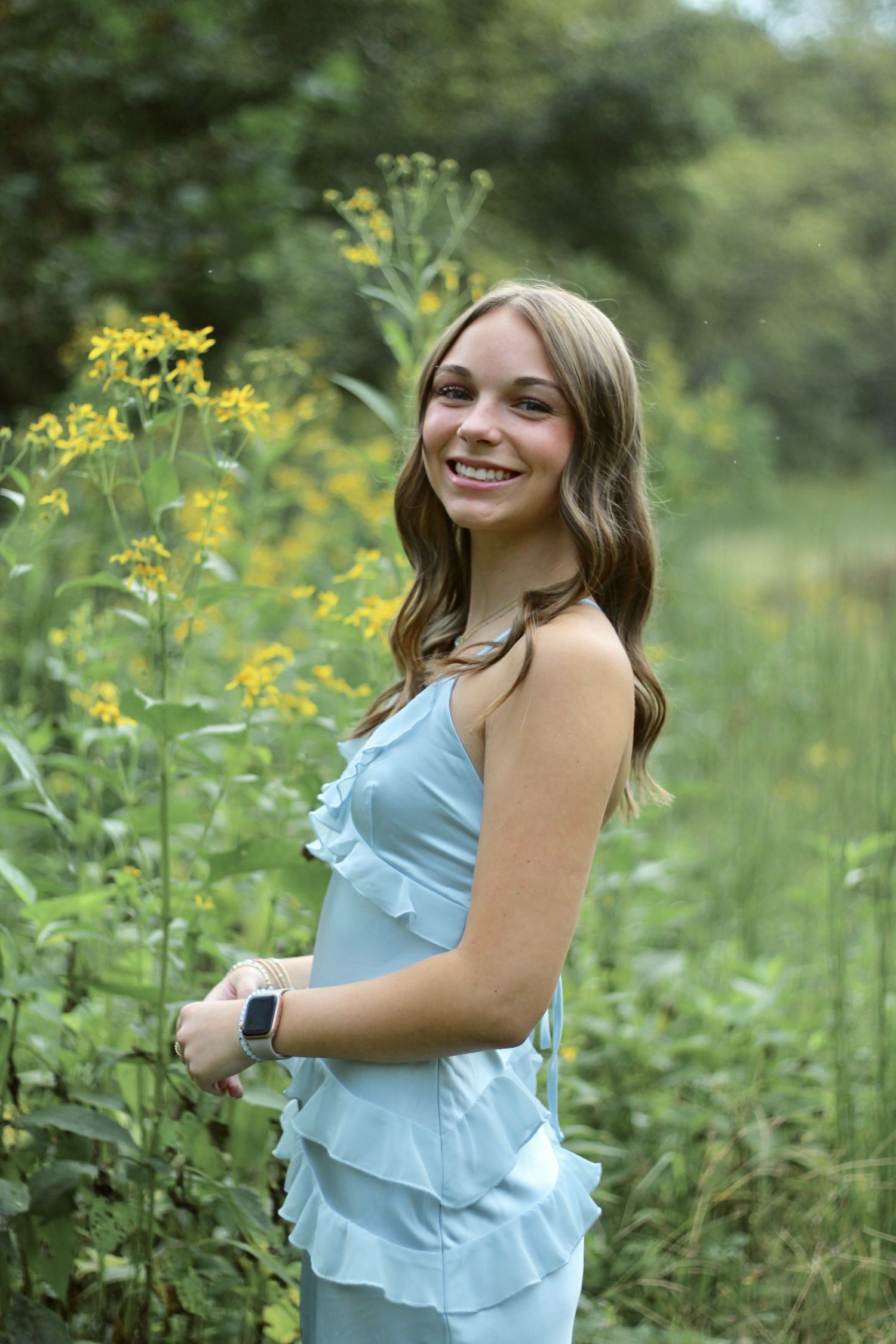 Surrounded by yellow flowers, she smiles at the camera in her gorgeous blue dress.