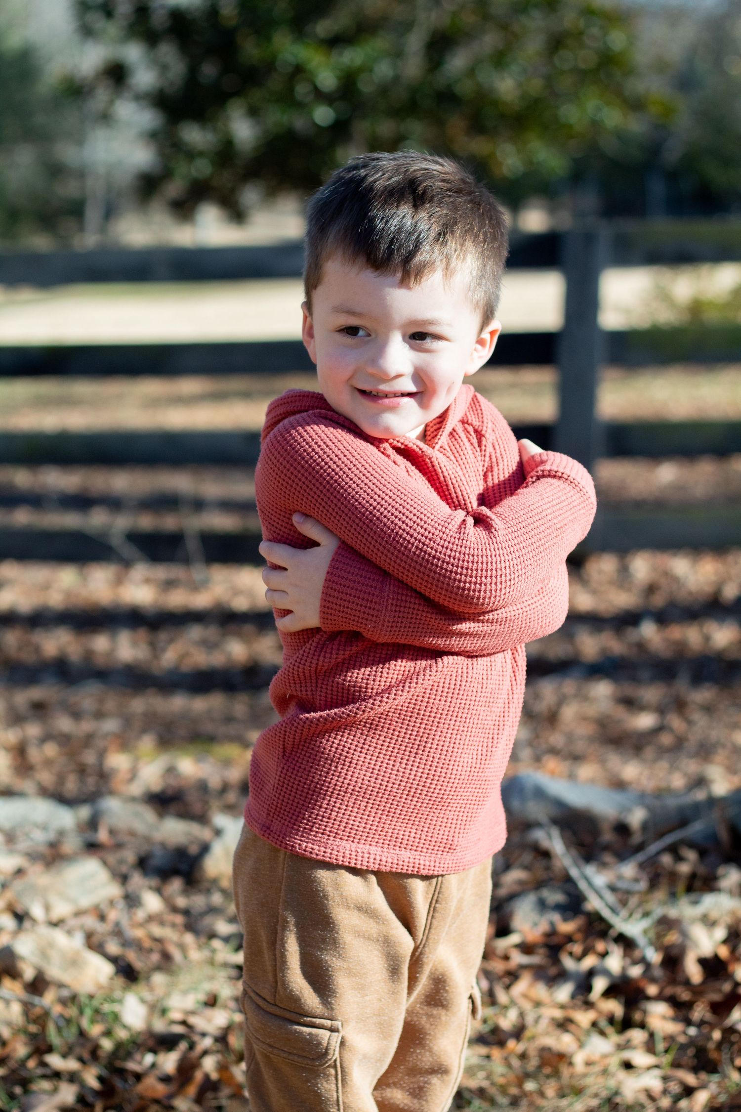 Young boy hugging himself and smiling sheepishly to the side.