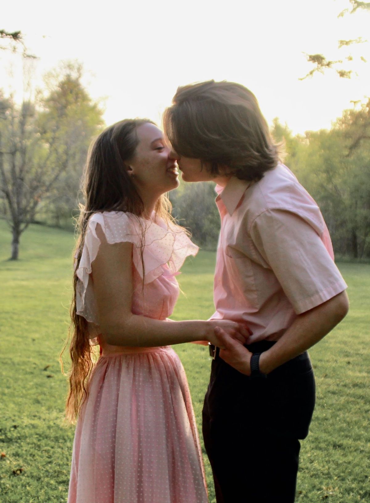 He bends to give her a kiss on the lips as the golden hour sun blossoms behind them.