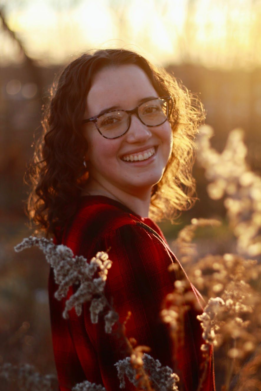 The golden hour sunshine giving her a face a glow, she smiles at the camera.