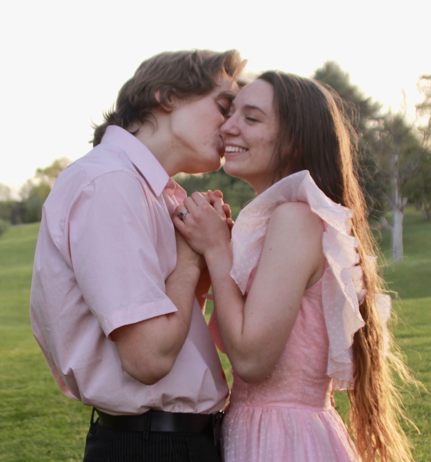 The Golden hour sunshine radiating around them, the guy moves to kiss his fiancee.