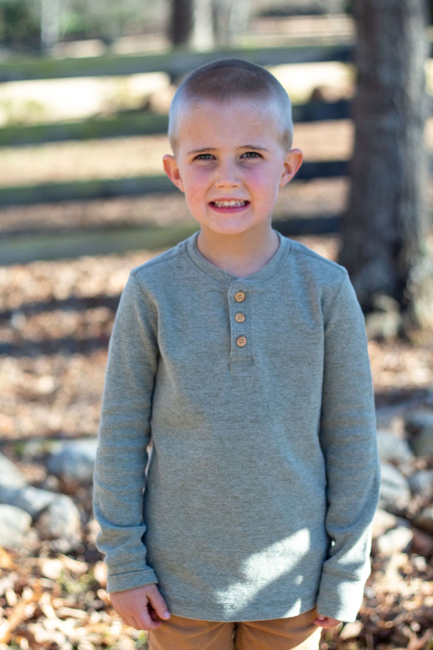 Little guy smiling in front of a fence and woodsy background.