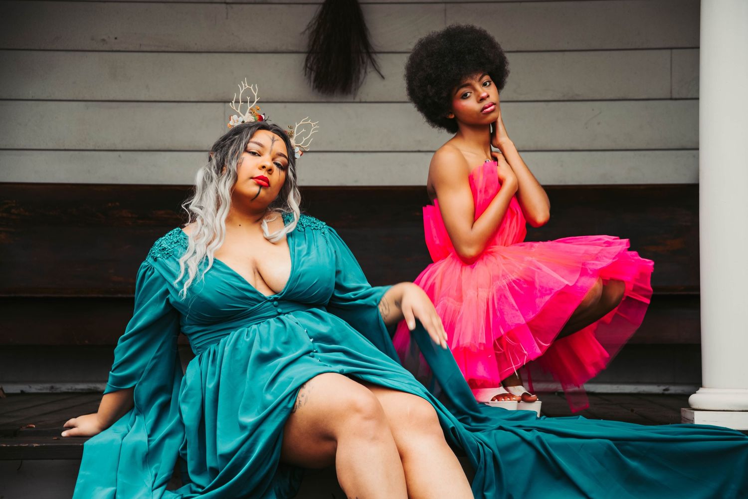 Two women in vibrant dresses pose on steps, one in teal velvet, the other in hot pink tulle.