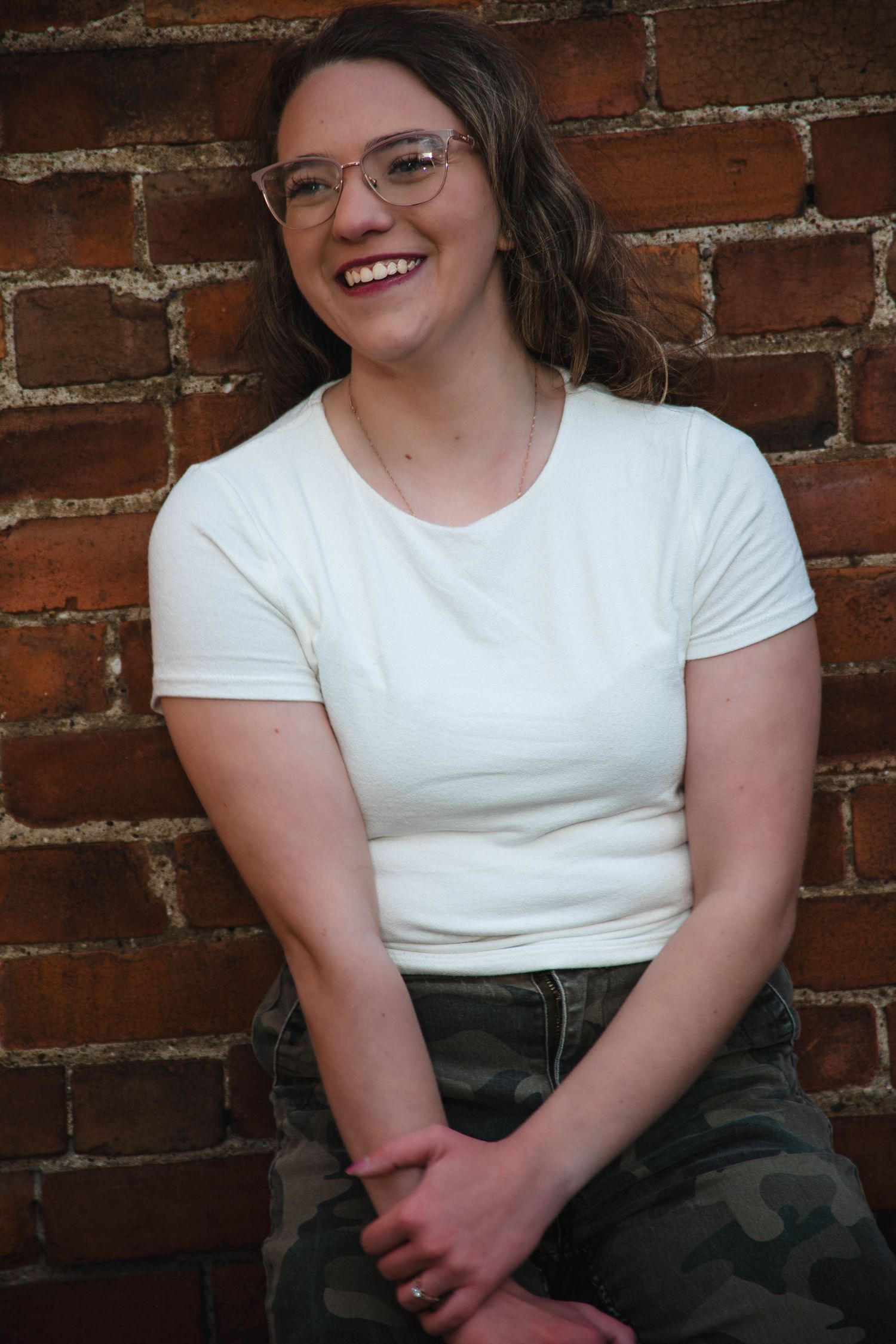 A series of candid portraits against a brick wall shows someone in a white t-shirt and glasses smiling and laughing.