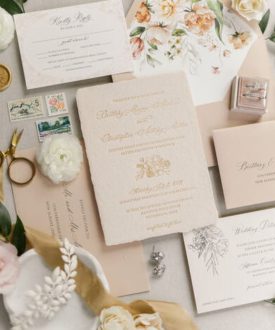 Elegant wedding invitation suite with blush floral designs, gold calligraphy and silk ribbon styled with white roses.