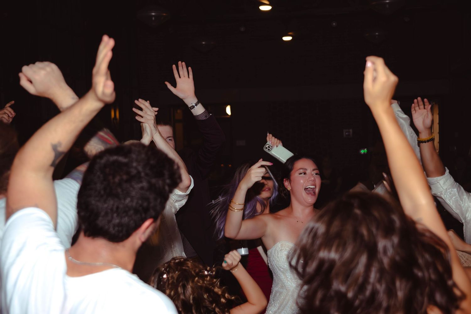 A dark concert venue filled with people raising their hands in excitement during a performance.