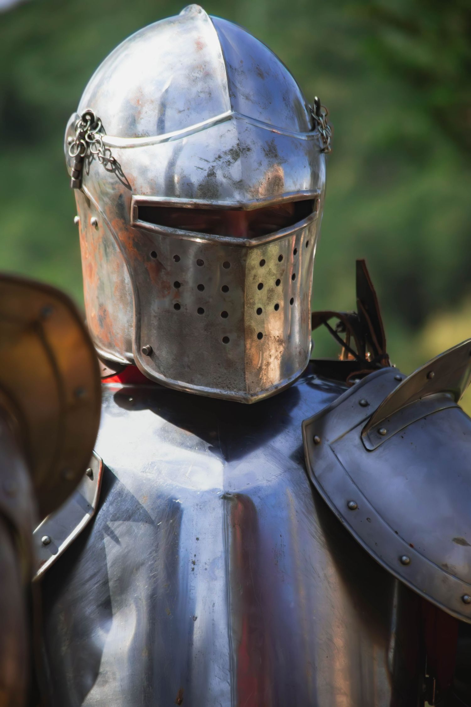 Close-up view of medieval knight's armor showing a shining steel helmet and shoulder plates in natural lighting.