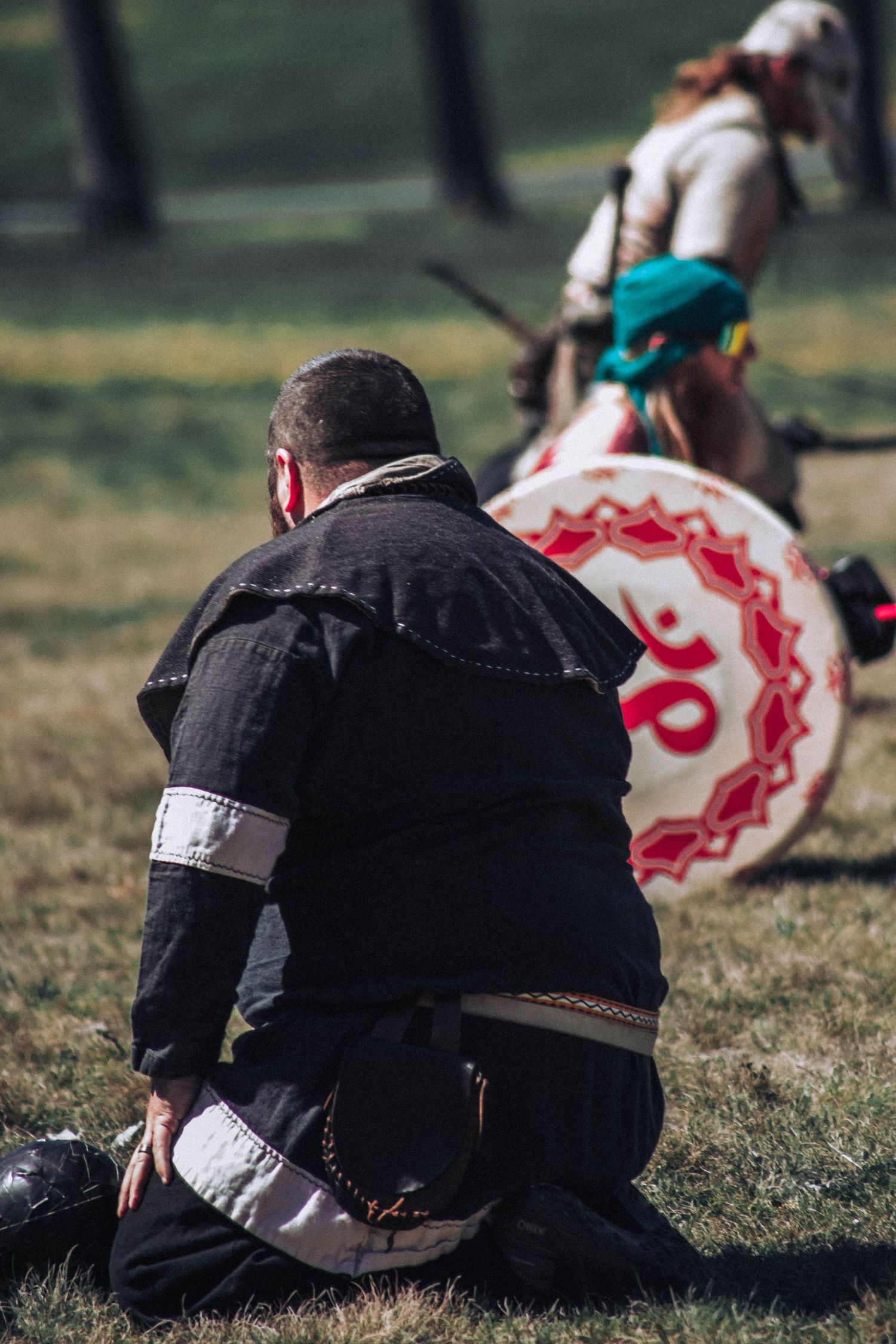 Medieval reenactors in black and white costumes rest on grassy field during outdoor historical event.