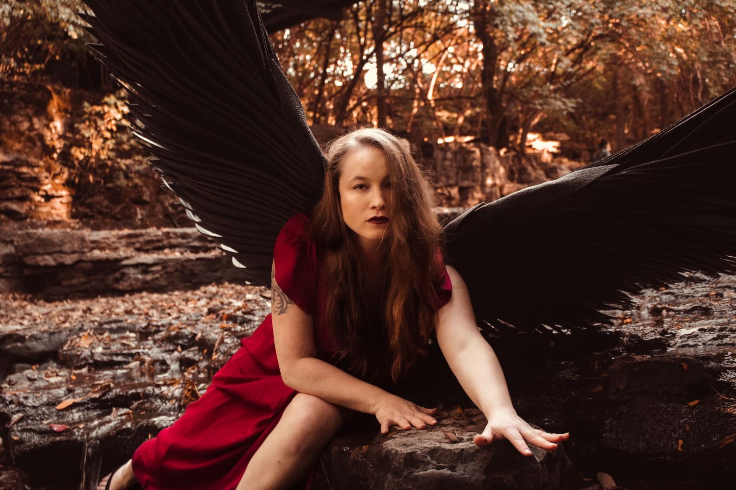 A person in a flowing red dress poses dramatically against a rocky outdoor backdrop during golden hour.