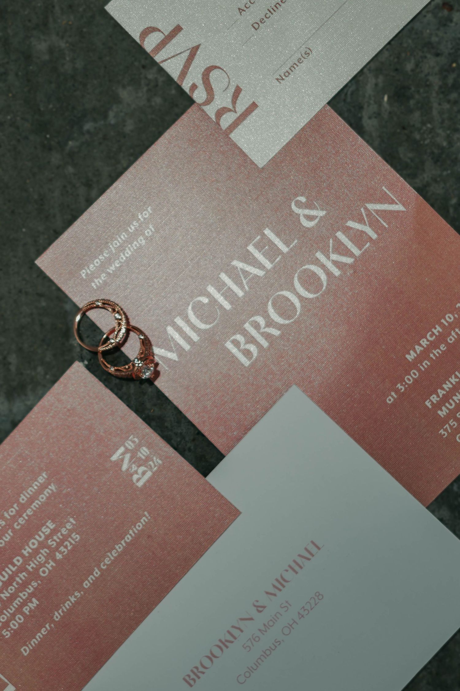 Angled view of minimalist business cards or invitations in soft pink and gray tones laid out on a dark surface.