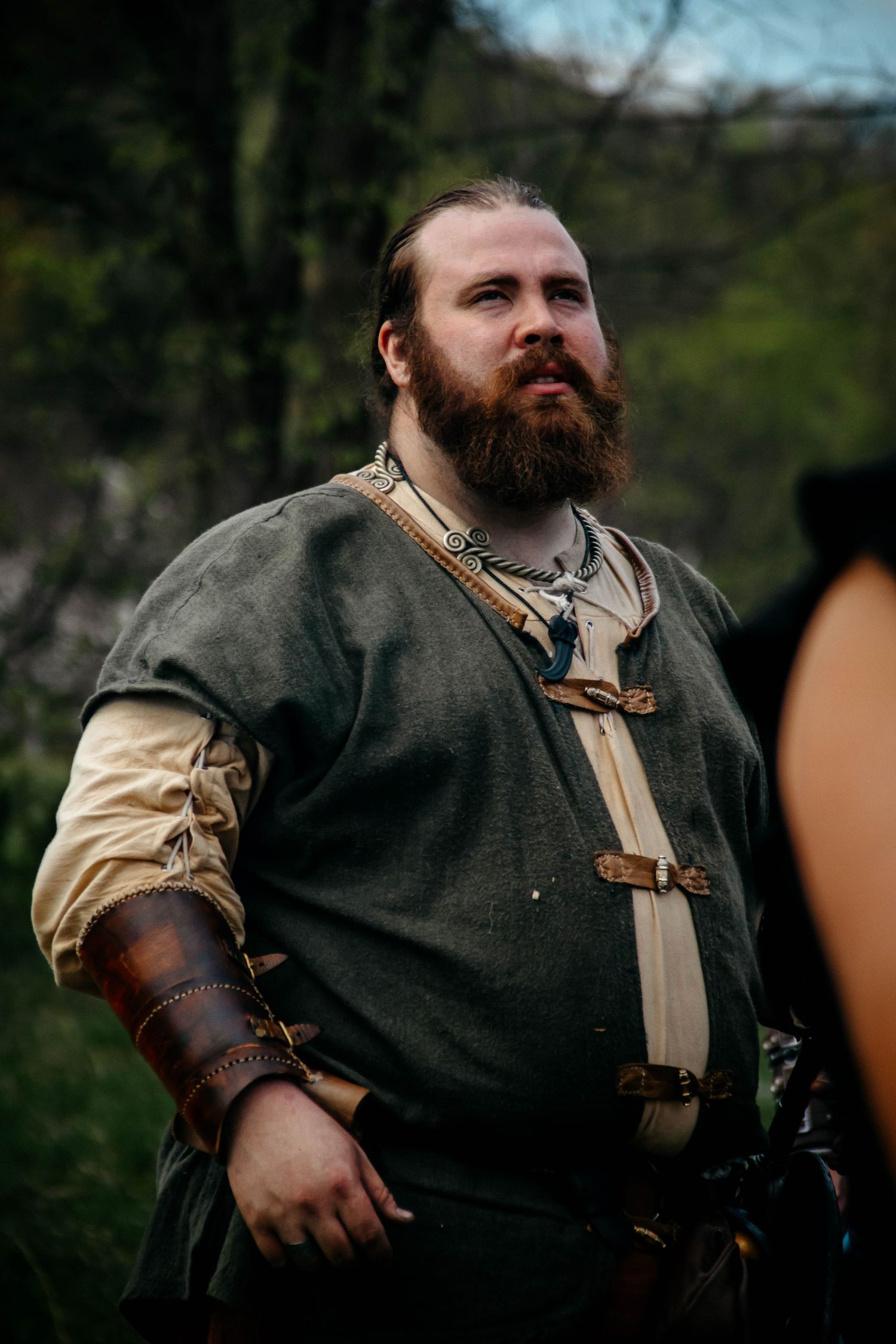 A reenactor in medieval garb with leather vest and white shirt stands in character.