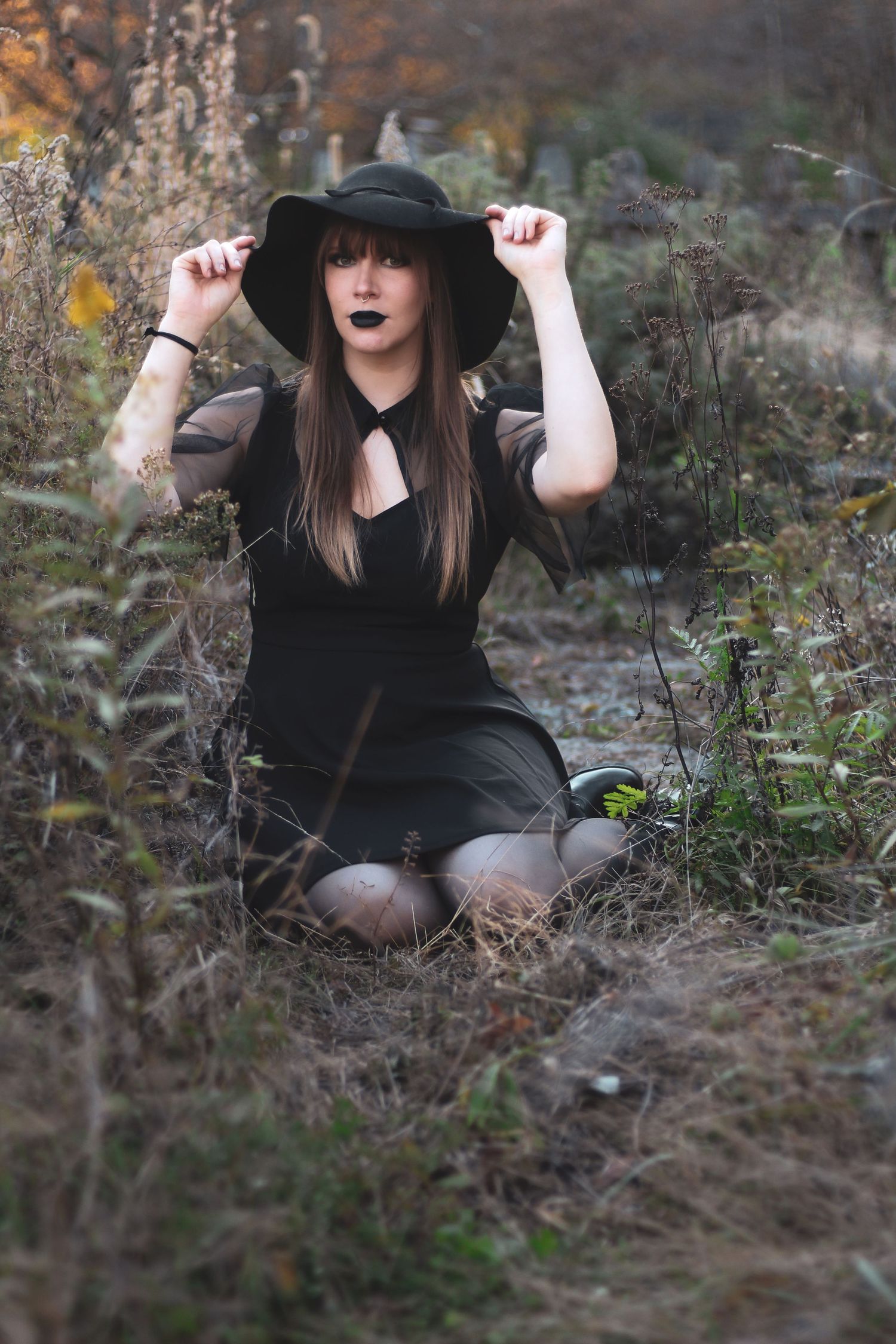 Gothic style portrait session with black clothing and hat in natural setting.